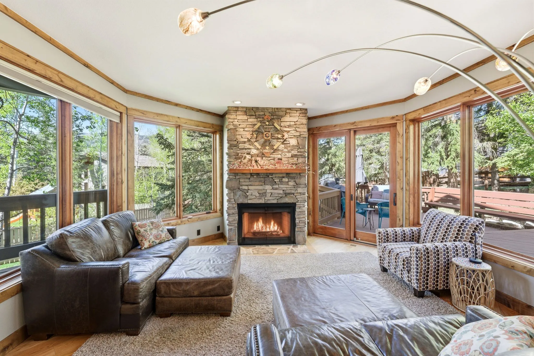 Living area featuring a stone-clad fireplace with a wood mantel, surrounded by large windows with wood trim