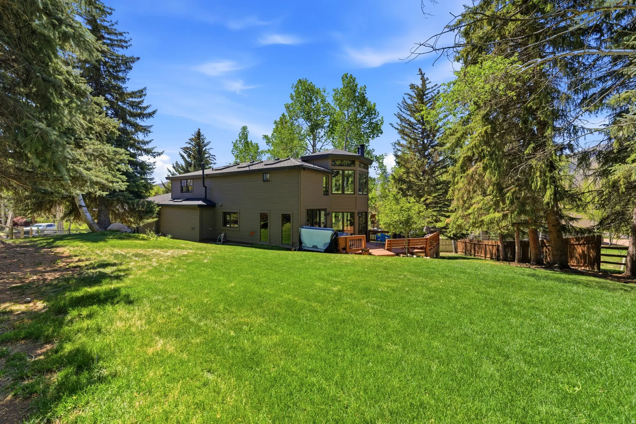 Expansive green lawn bordering a natural wood fence and mature evergreen trees