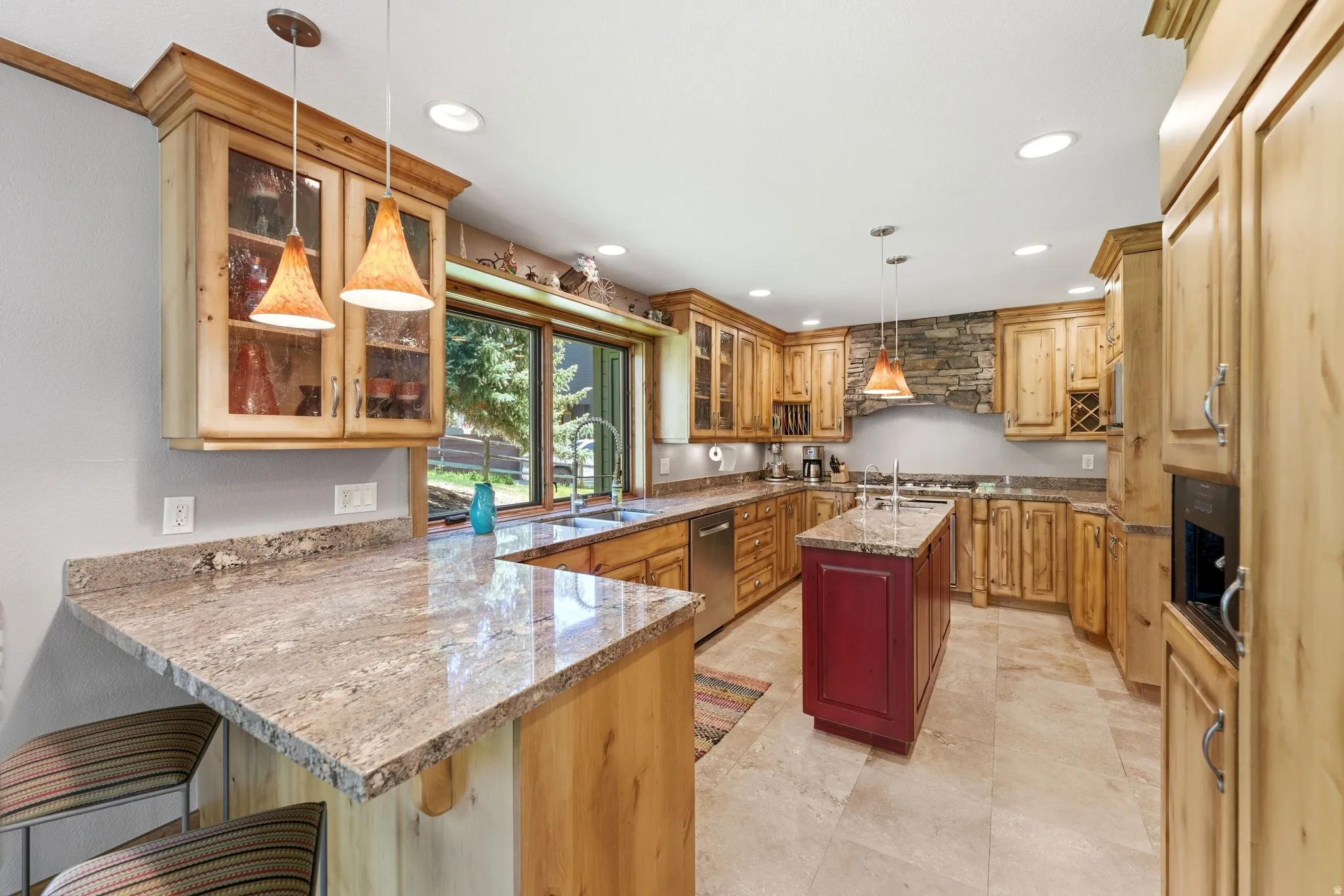 Spacious kitchen featuring extensive natural wood cabinetry, light-toned countertops, a contrasting red island, tile flooring, and integrated stainless steel appliances