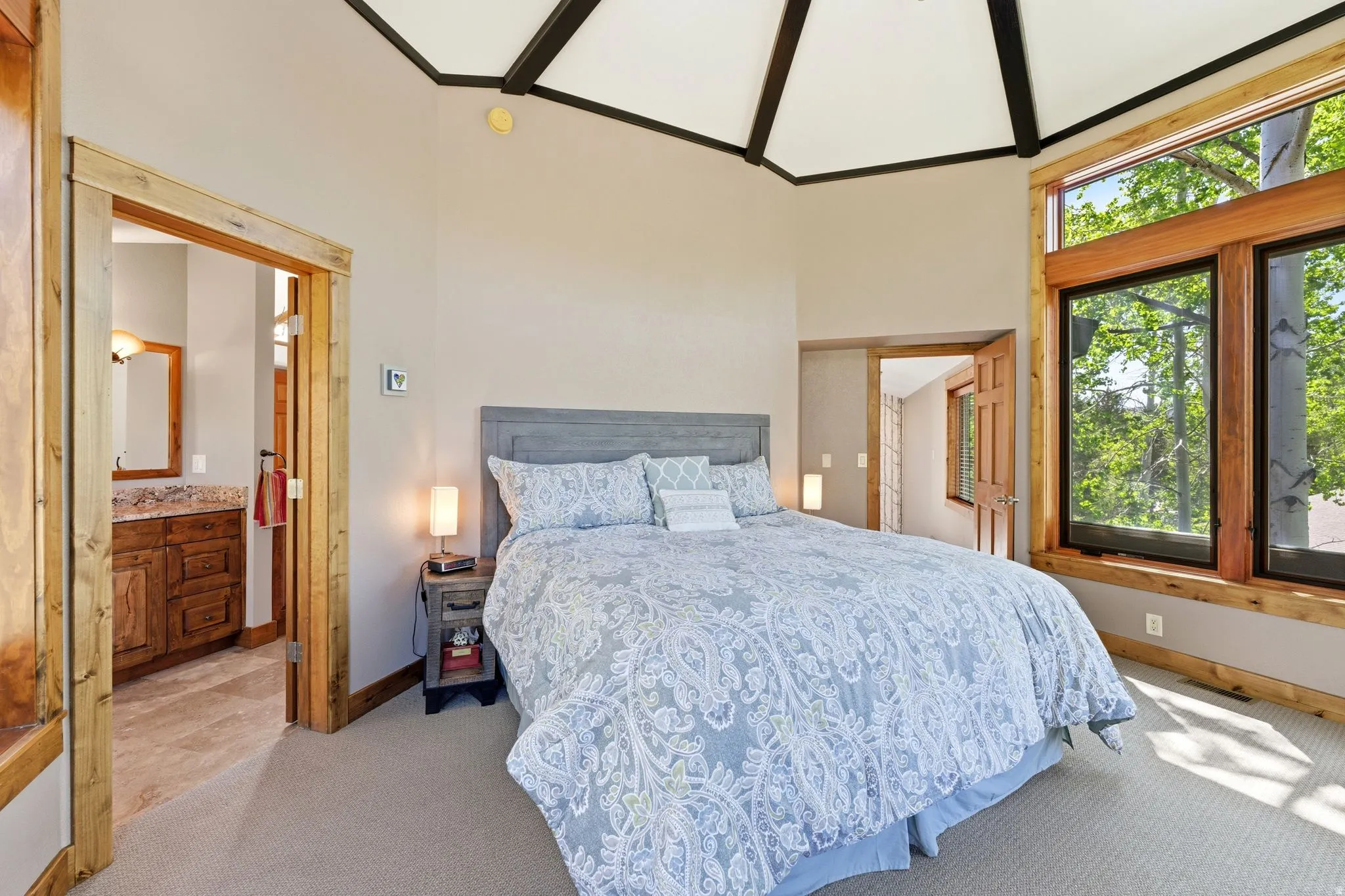 Bedroom featuring a vaulted ceiling with exposed beams, large windows with natural wood trim, and a carpeted floor