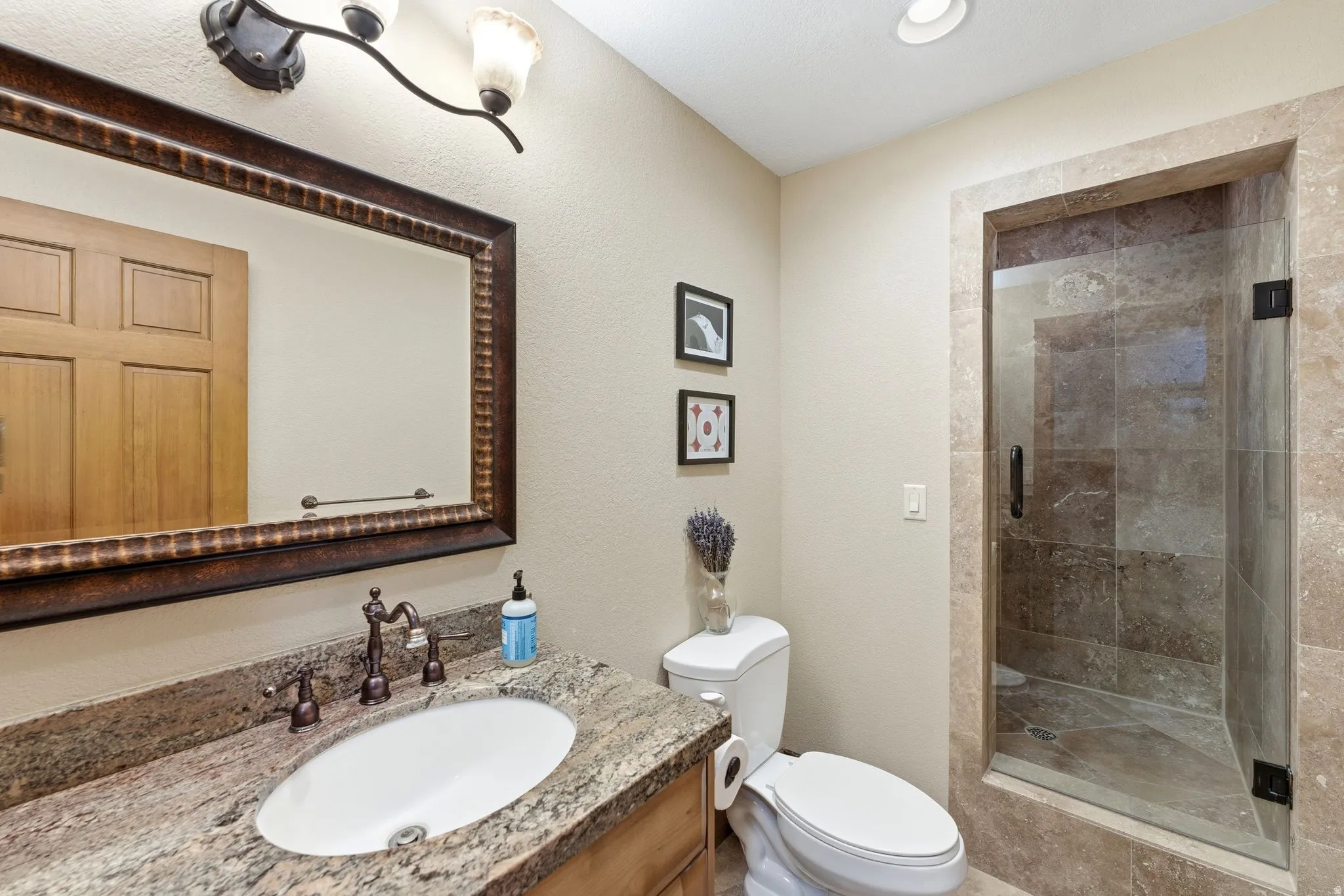 Bathroom featuring a framed mirror, granite countertop with undermount sink, bronze-finish fixtures, and a tiled shower with a glass enclosure