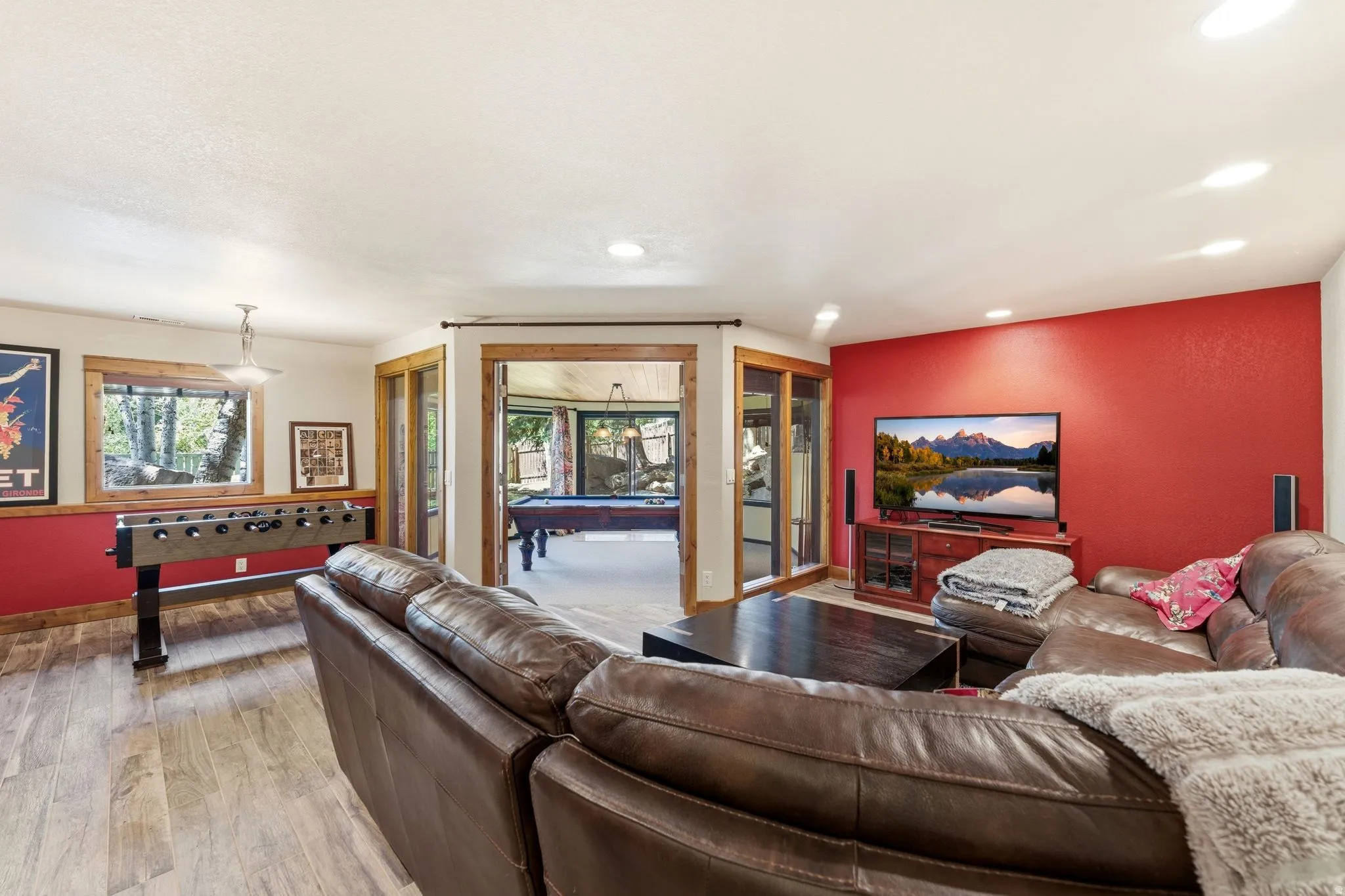 Spacious entertainment area featuring wood-finish flooring, a vibrant accent wall, recessed lighting, and large windows with natural wood trim
