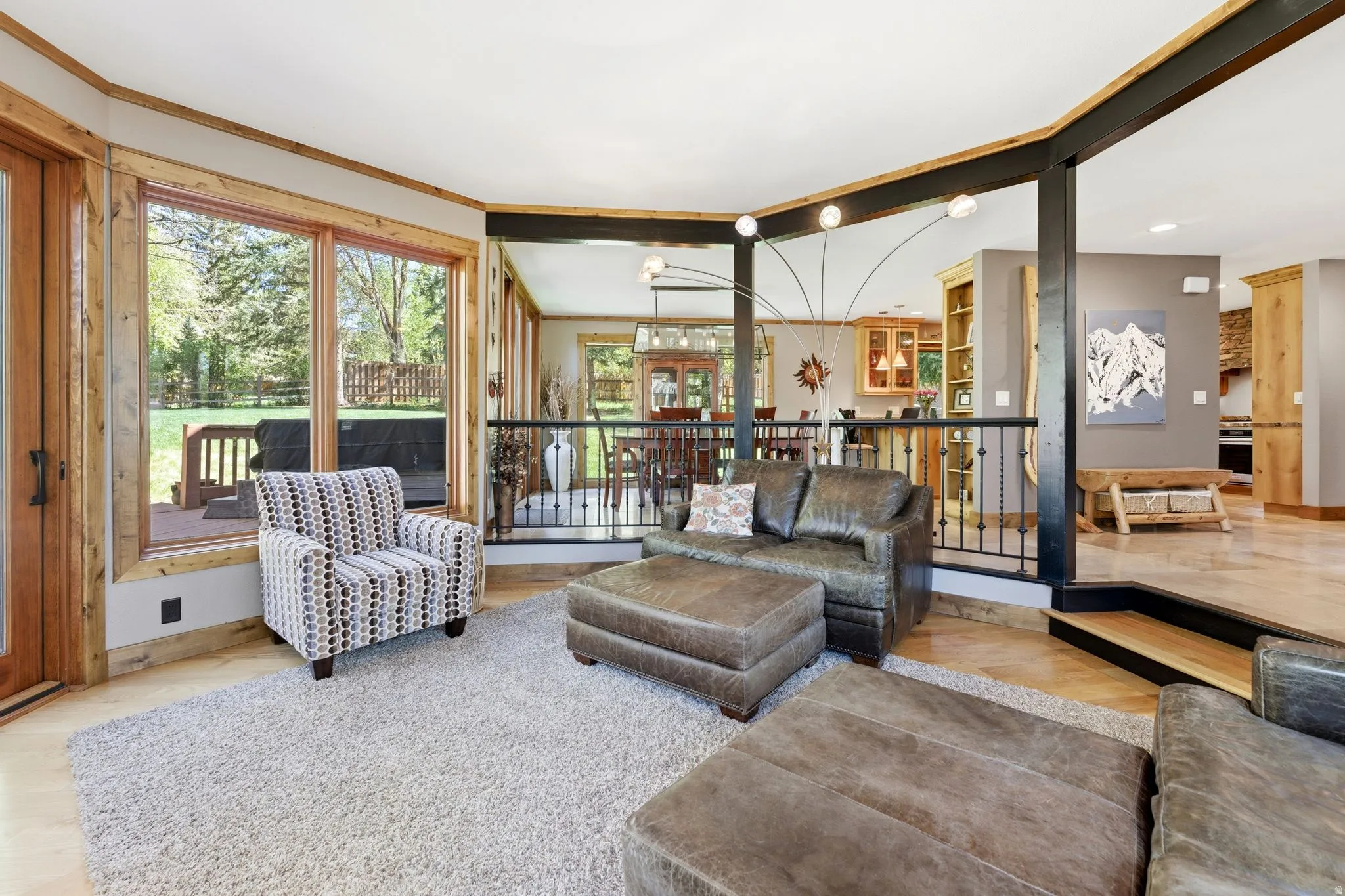 Open-concept living area featuring light wood-finish flooring, a neutral-toned area rug, and a perimeter of natural wood trim