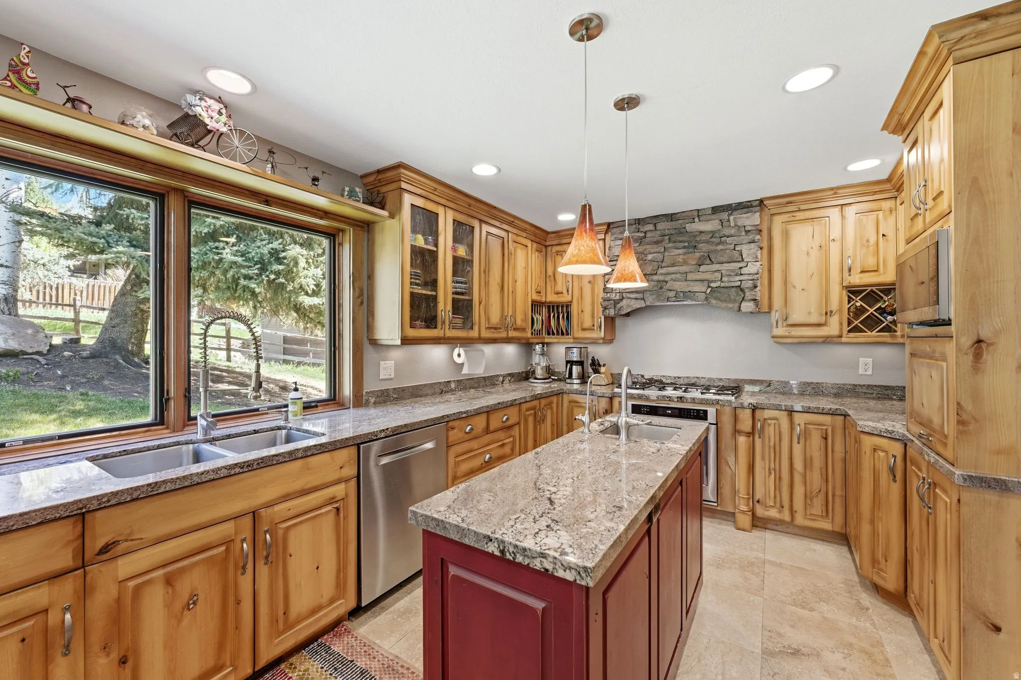Gourmet kitchen featuring custom wood cabinetry, stone countertops, a large center island with pendant lighting, a built-in wine rack, and a stone-clad range hood