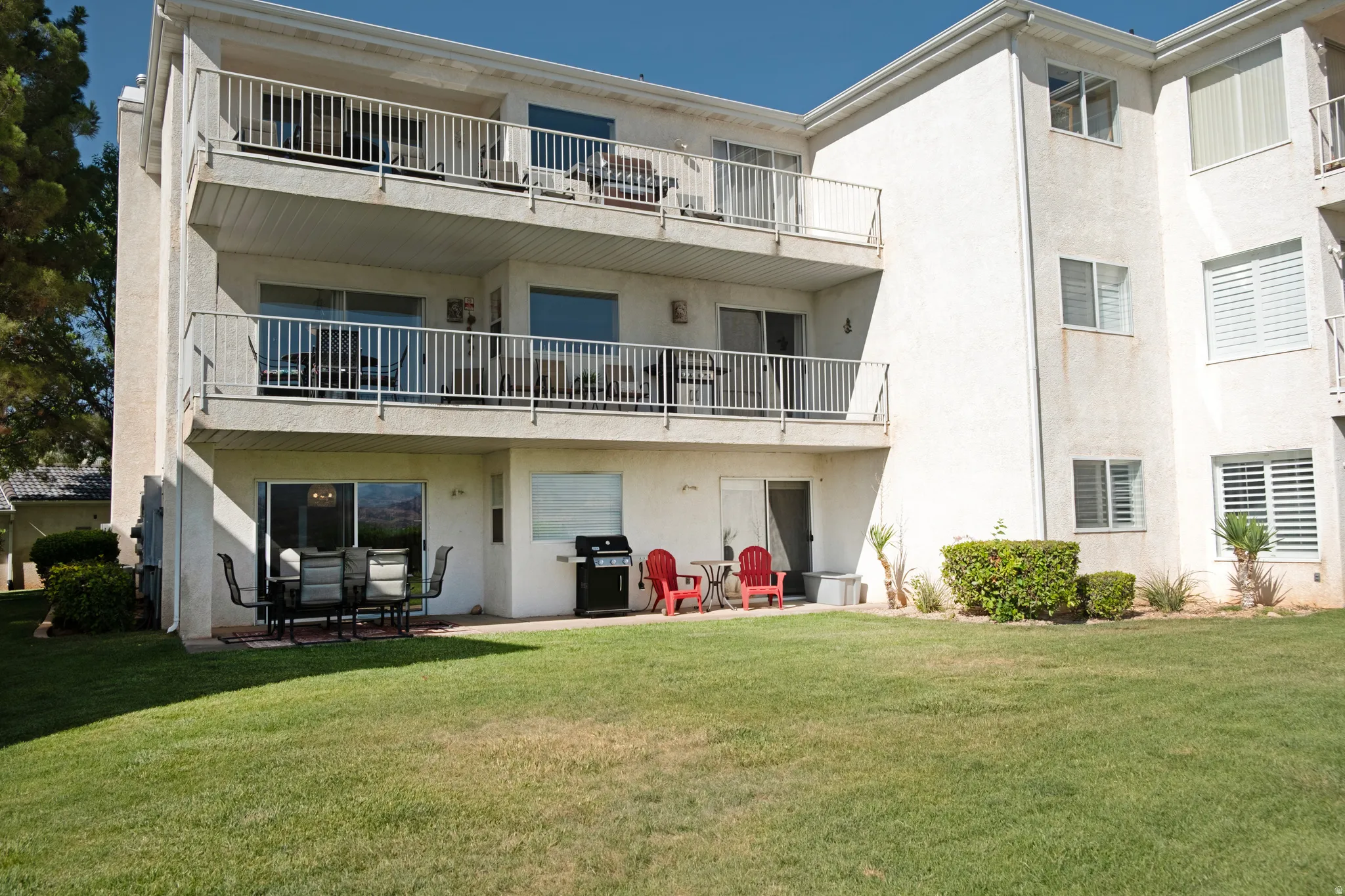 Multi-story building featuring private balconies, ground-level patio space, sliding glass doors, and manicured lawn areas
