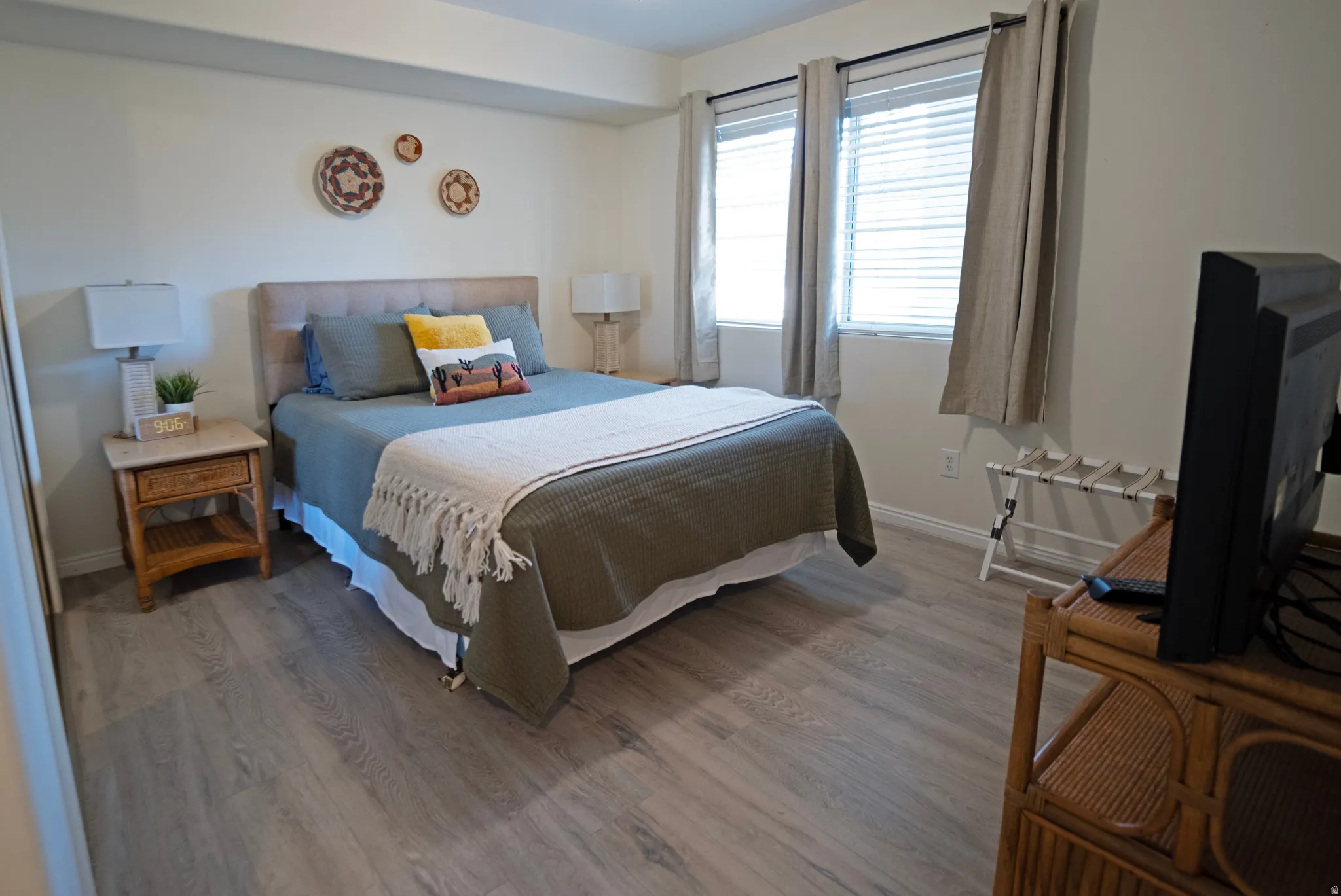 Bedroom featuring wood-finish flooring, neutral wall tones, and two windows with blinds and drapes
