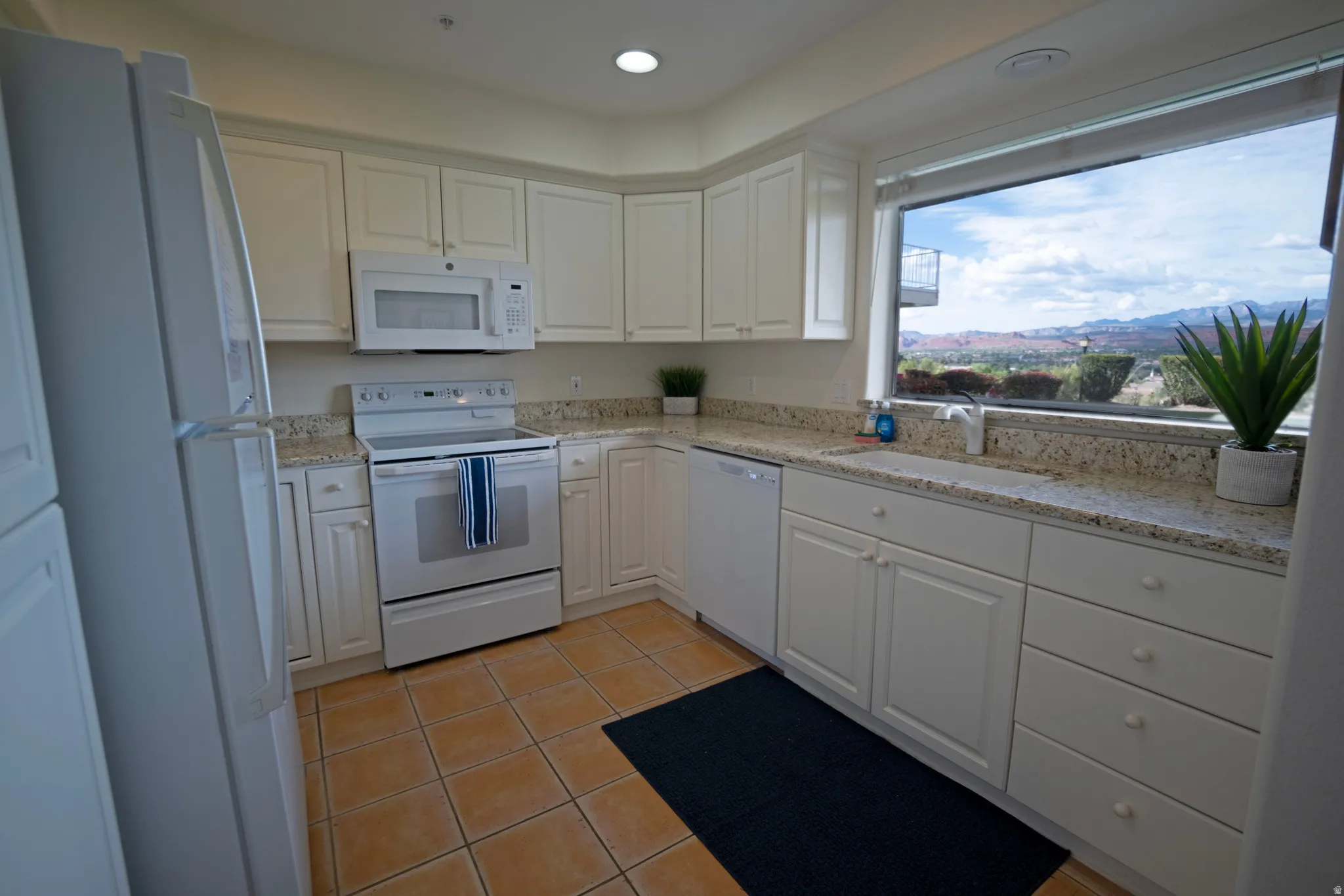 Kitchen featuring a large picture window, white cabinetry with round knobs, light granite countertops, and tile flooring