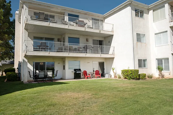 Multi-story building featuring private balconies, ground-level patio space, sliding glass doors, and manicured lawn areas