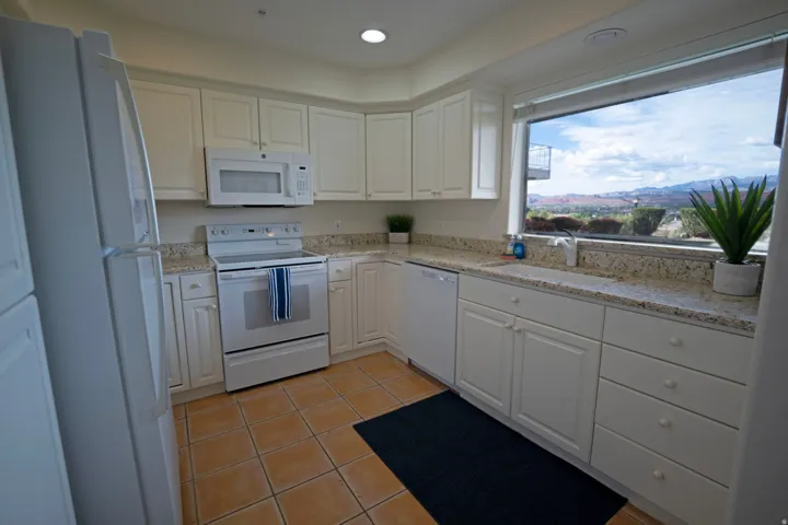 Kitchen featuring a large picture window, white cabinetry with round knobs, light granite countertops, and tile flooring