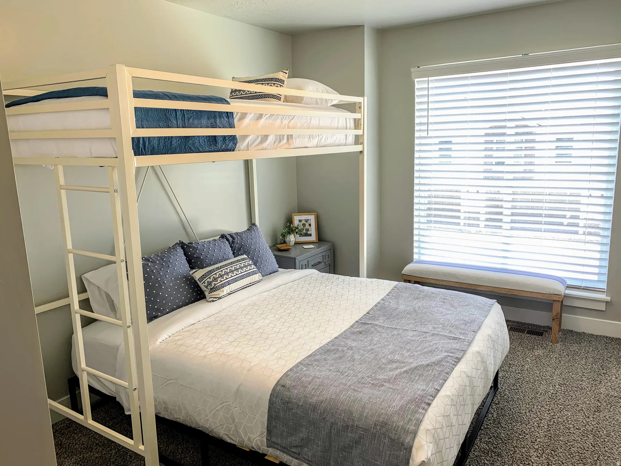 Bedroom featuring a metal bunk bed frame with integrated ladder, a large window with white horizontal blinds, and neutral-toned wall paint