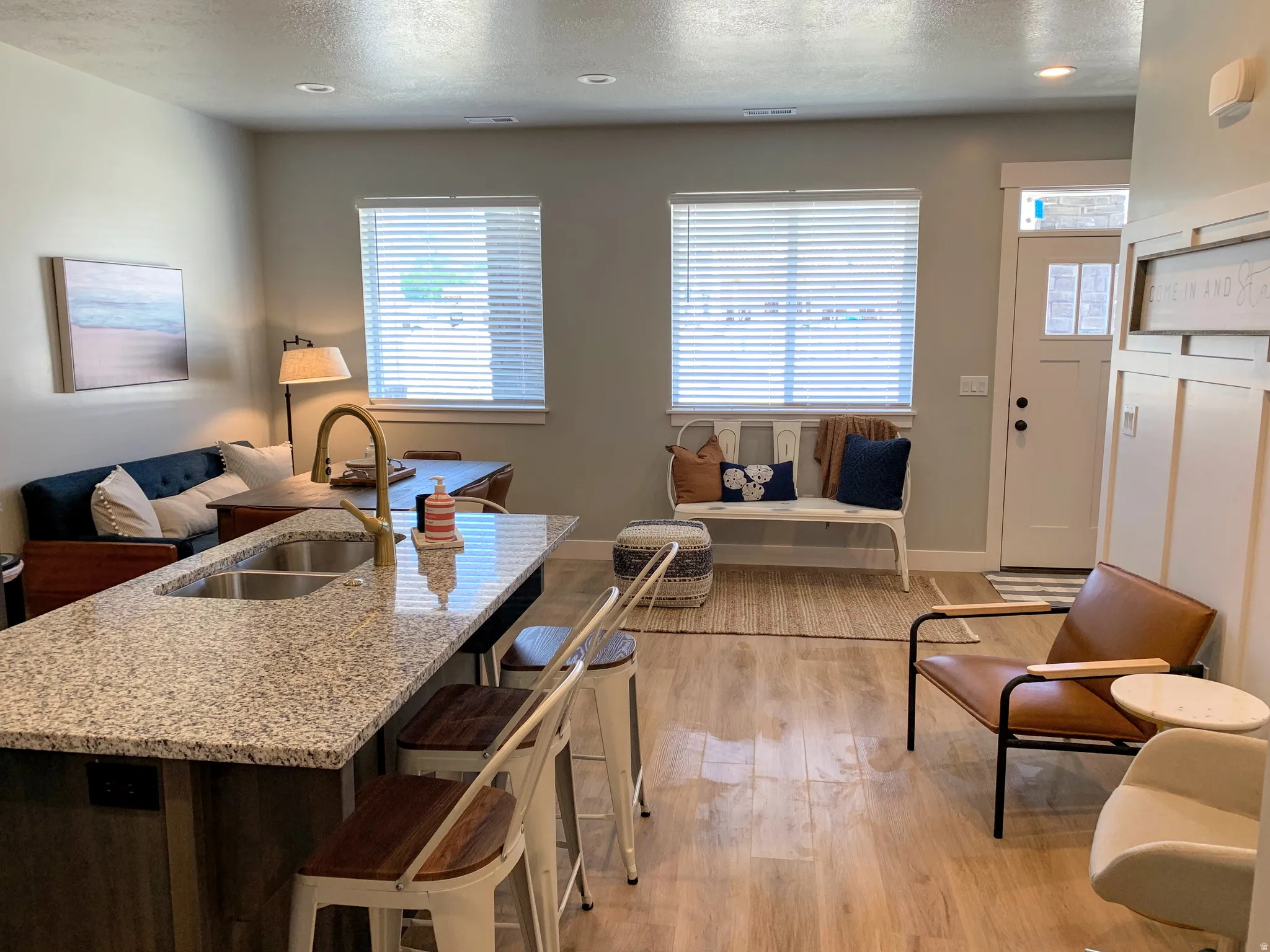 Contemporary open-concept living area featuring wood-finish flooring, a kitchen island with a double basin sink and stone-finish countertop, and recessed lighting