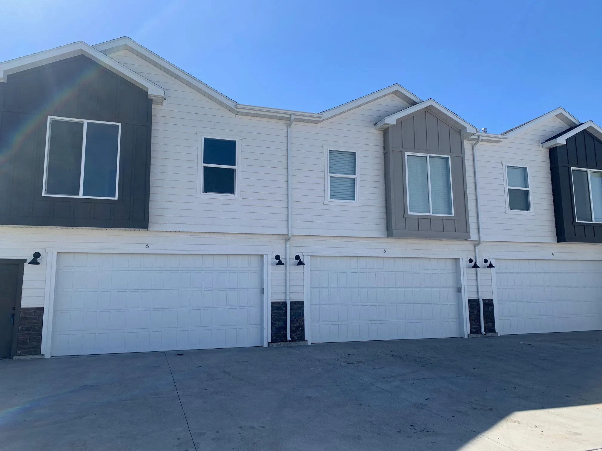 Contemporary multi-unit exterior featuring contrasting horizontal and vertical siding, multiple white panel garage doors, and black-finish exterior sconces