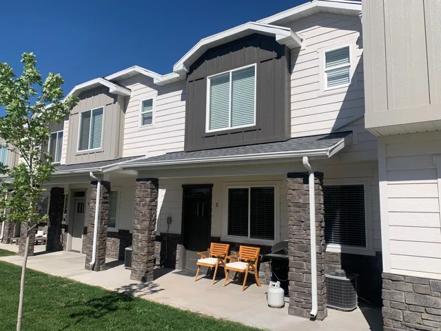 Exterior facade featuring stacked stone columns, light-colored horizontal siding, and dark vertical siding accents