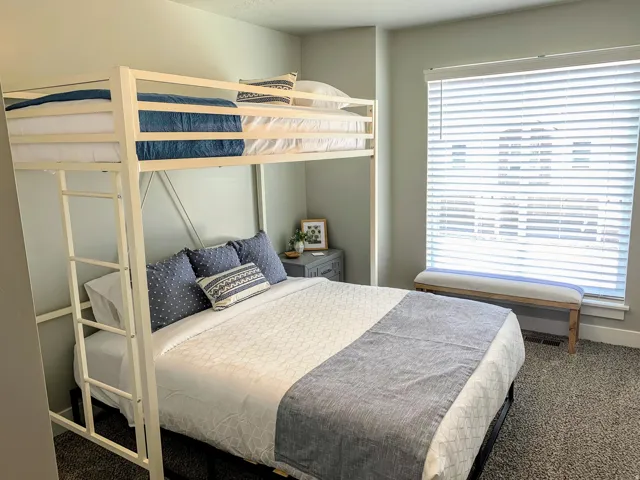 Bedroom featuring a metal bunk bed frame with integrated ladder, a large window with white horizontal blinds, and neutral-toned wall paint