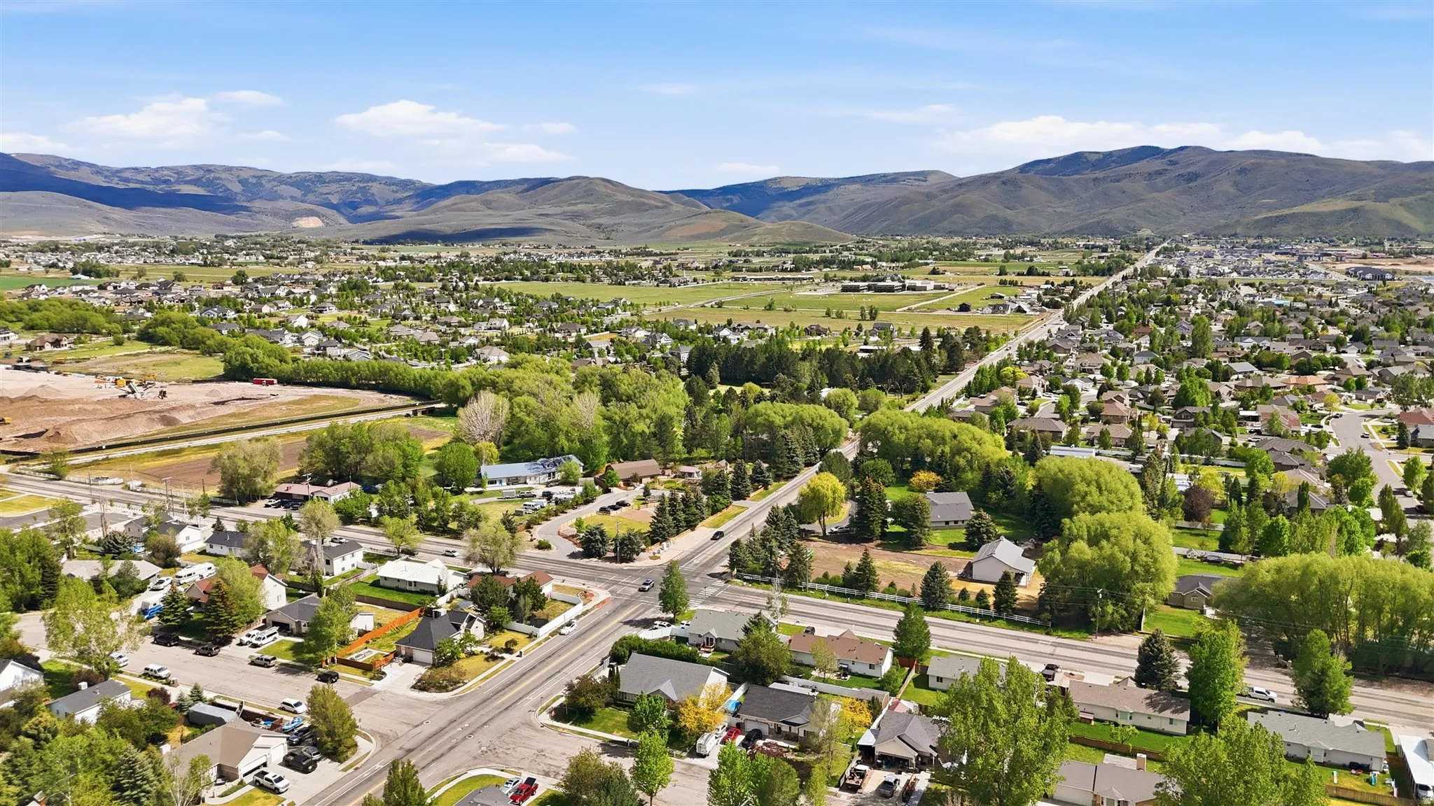 Expansive aerial perspective showcasing a residential community with mature trees and paved roadways, set against a backdrop of rolling hills and mountains