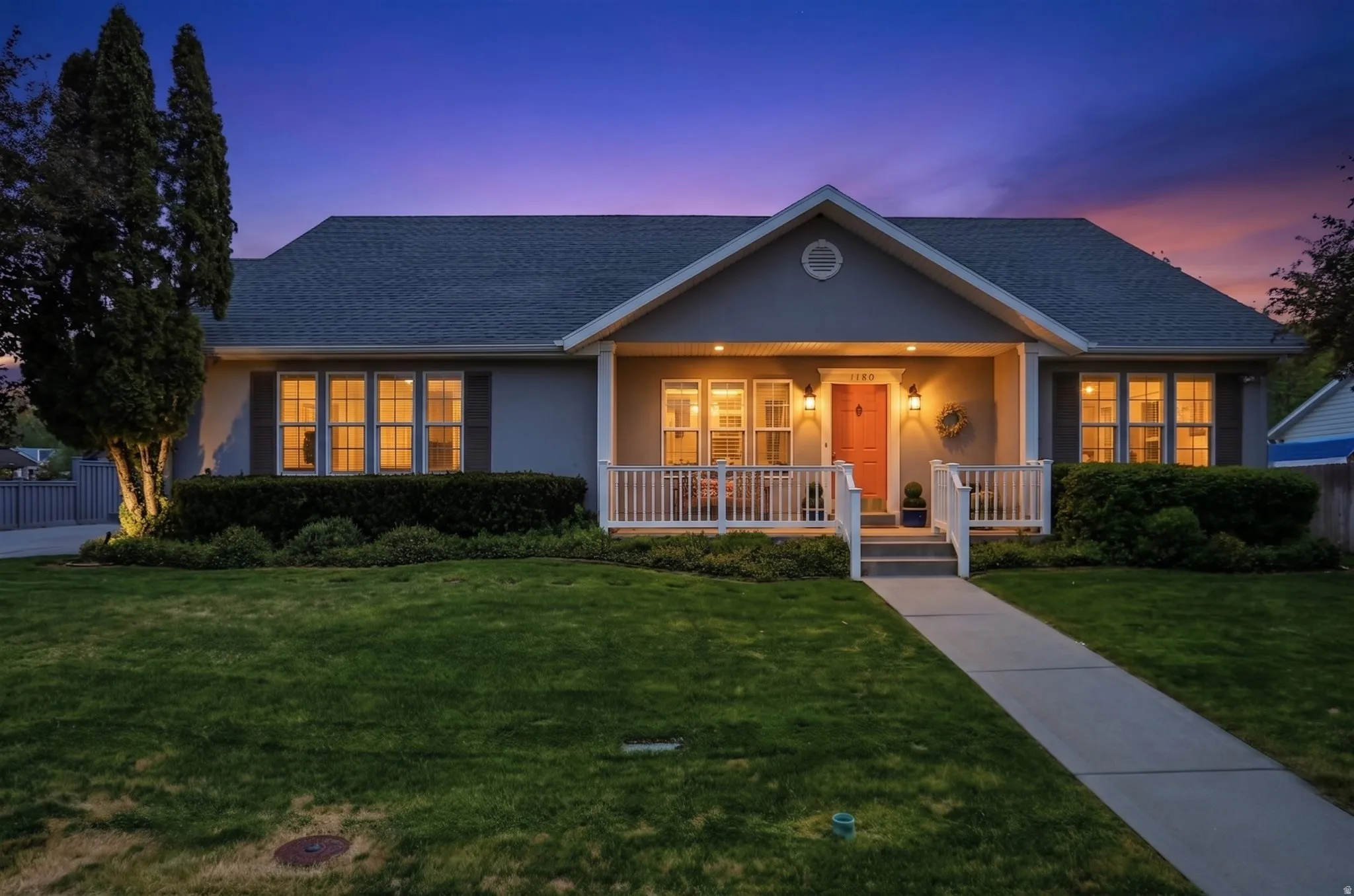Rambler style home featuring a covered front porch with white railings, a contrasting pink entry door, and grey siding