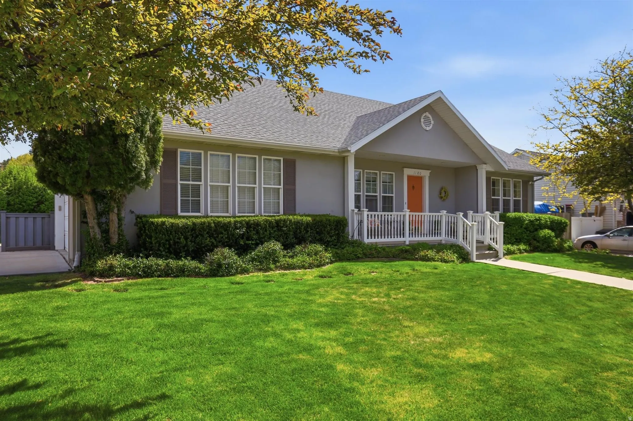 Single-story residence featuring a covered front porch, an orange entry door, white railings, and a gray exterior finish