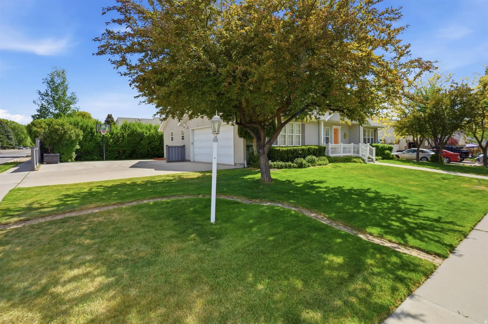 Expansive front yard featuring a verdant lawn, mature shade trees, a concrete driveway, and a two-car garage