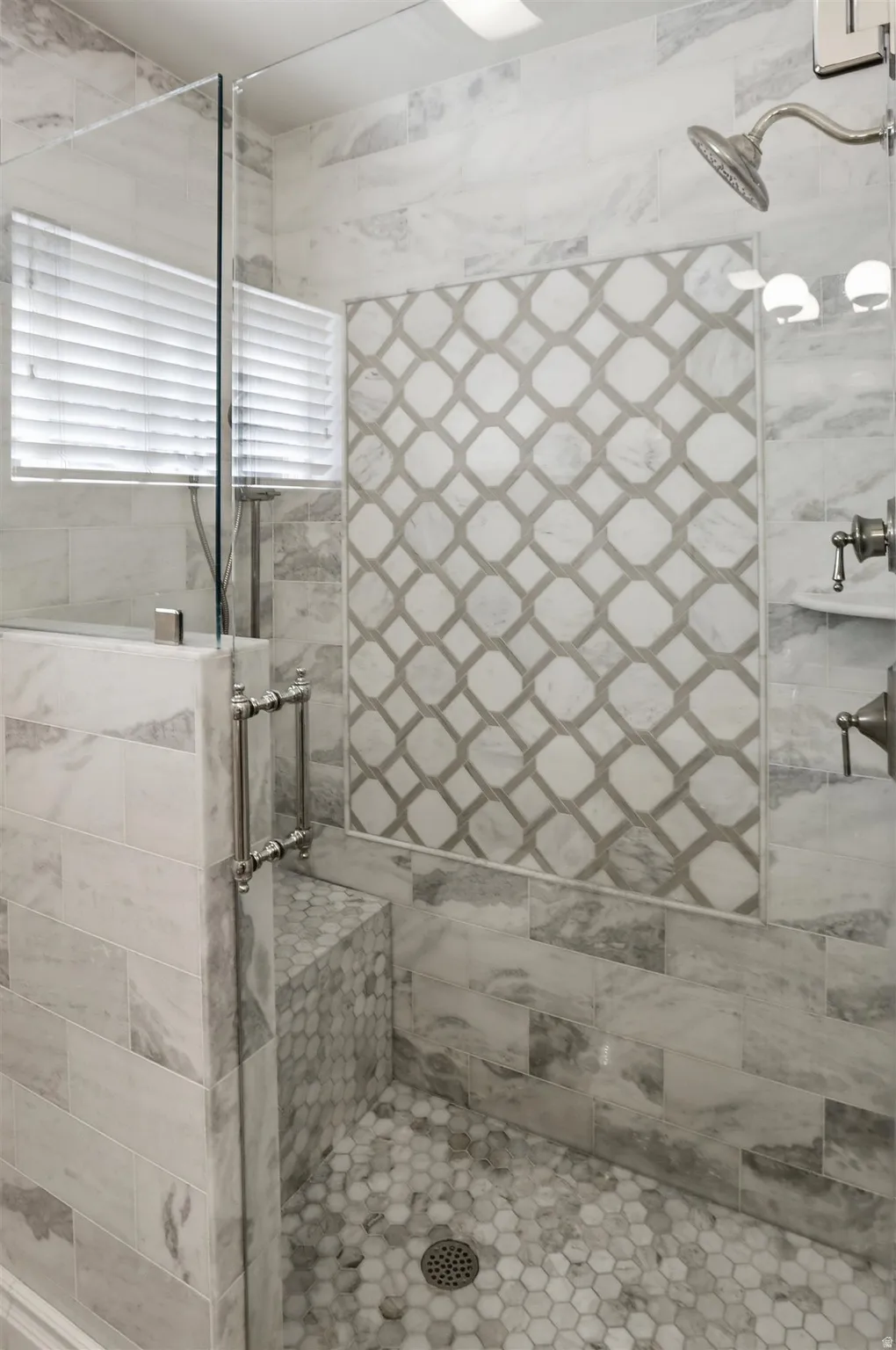 Shower enclosure with clear glass door, built-in bench, and hexagon tile floor