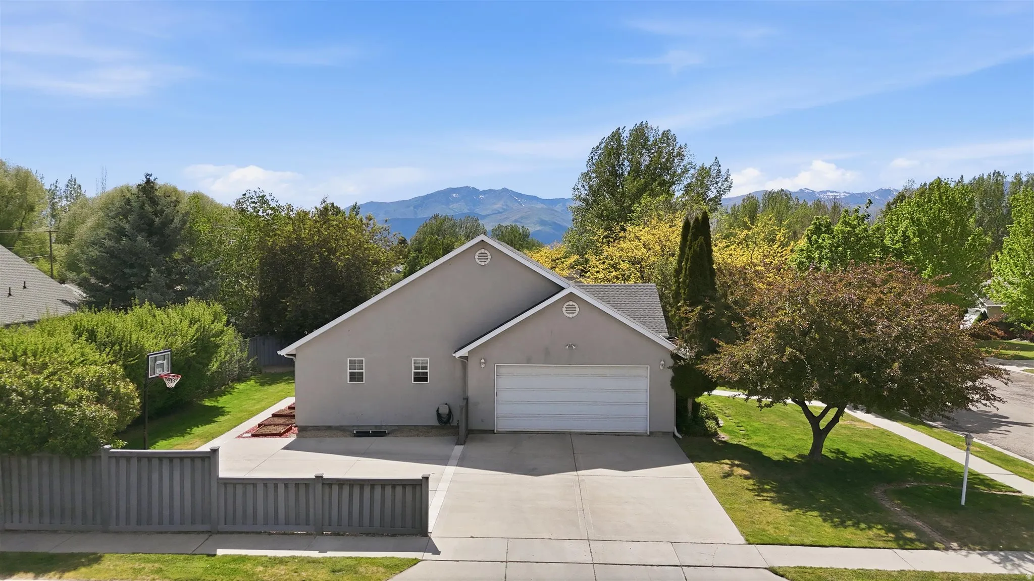 Contemporary stucco exterior featuring an attached two-car garage, mature trees, and a concrete driveway