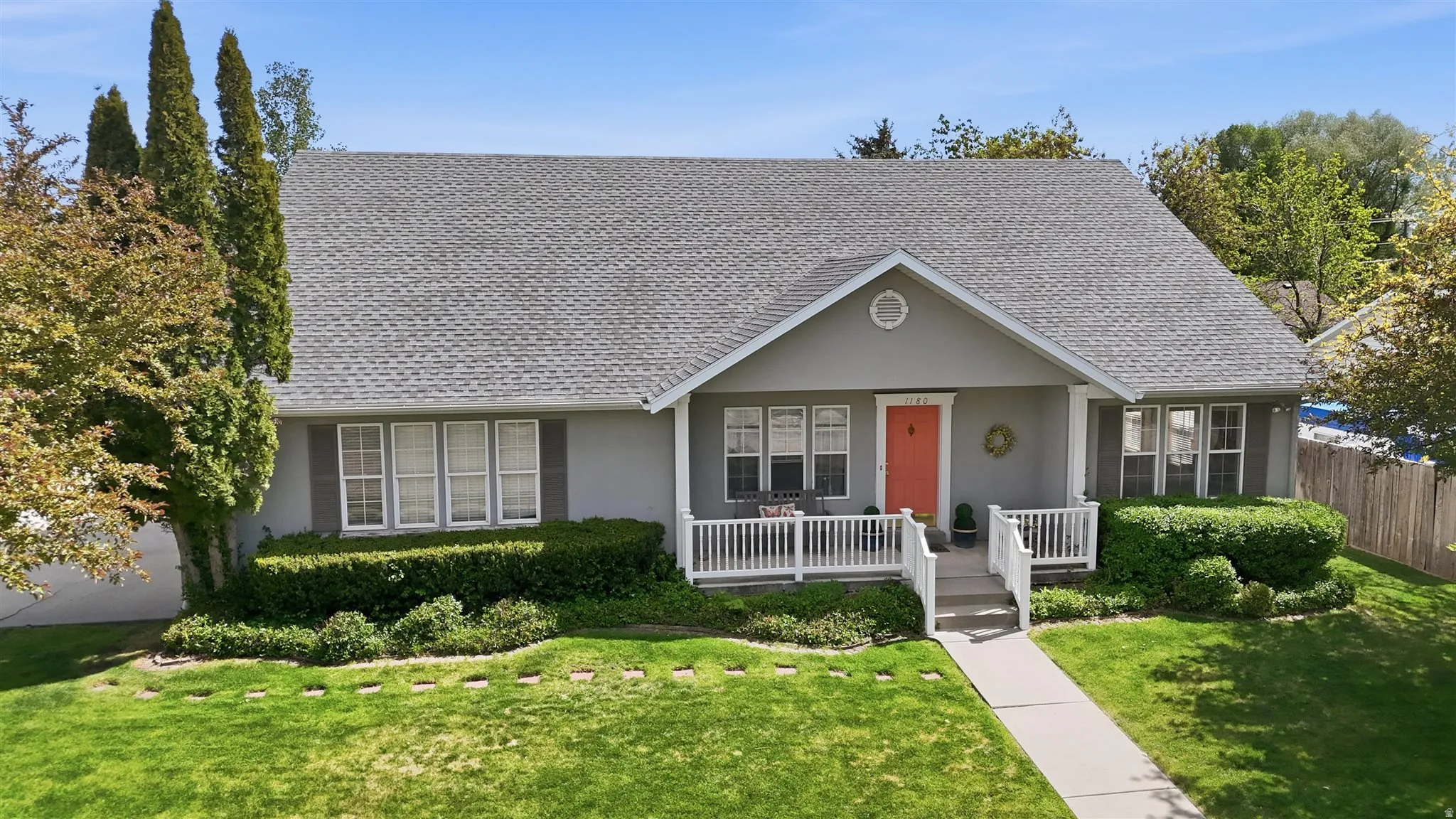 Rambler, stucco exterior, high pitched roof residence featuring a covered front porch with white railings