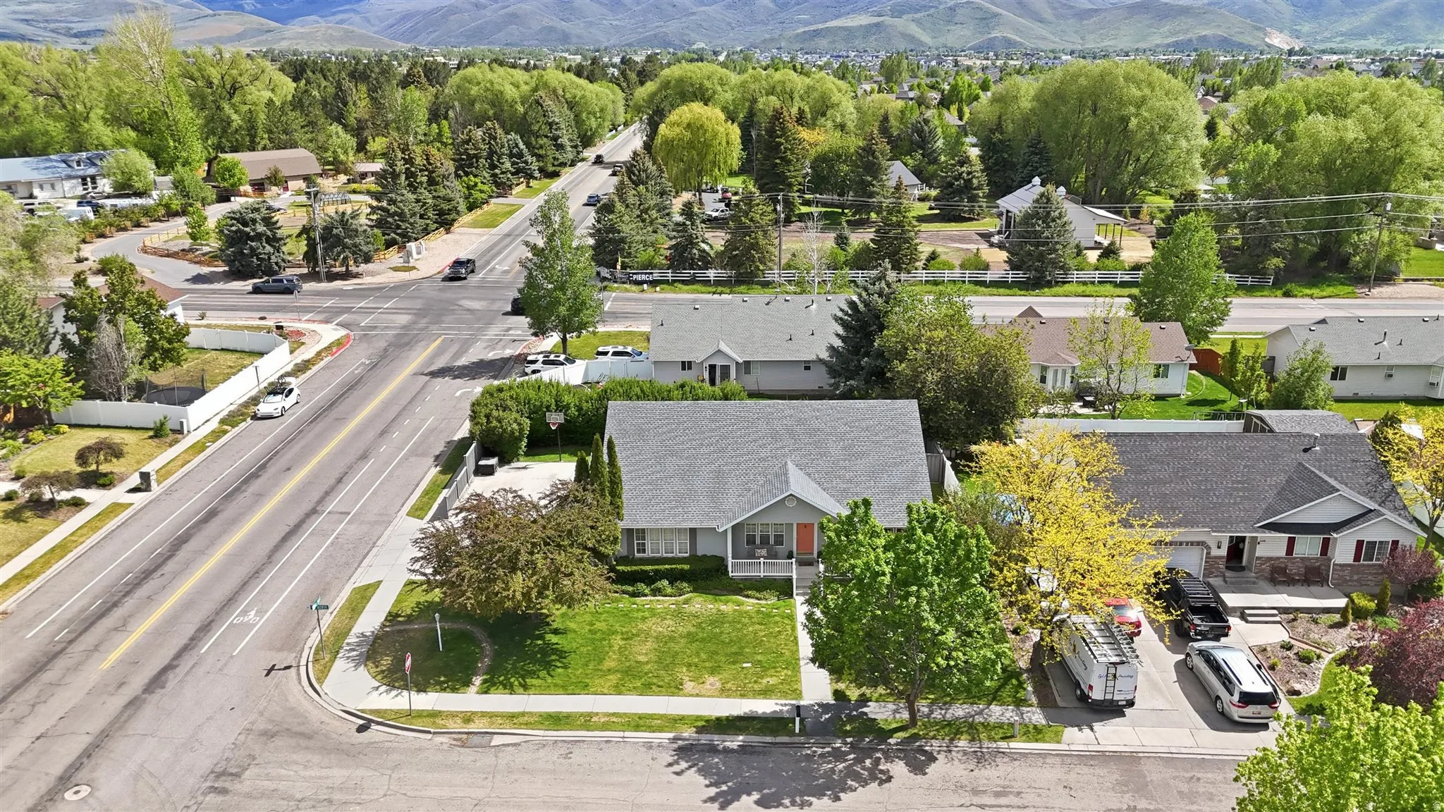 Corner lot property featuring a light gray exterior, a covered front porch with pink door, and a beautiful yard