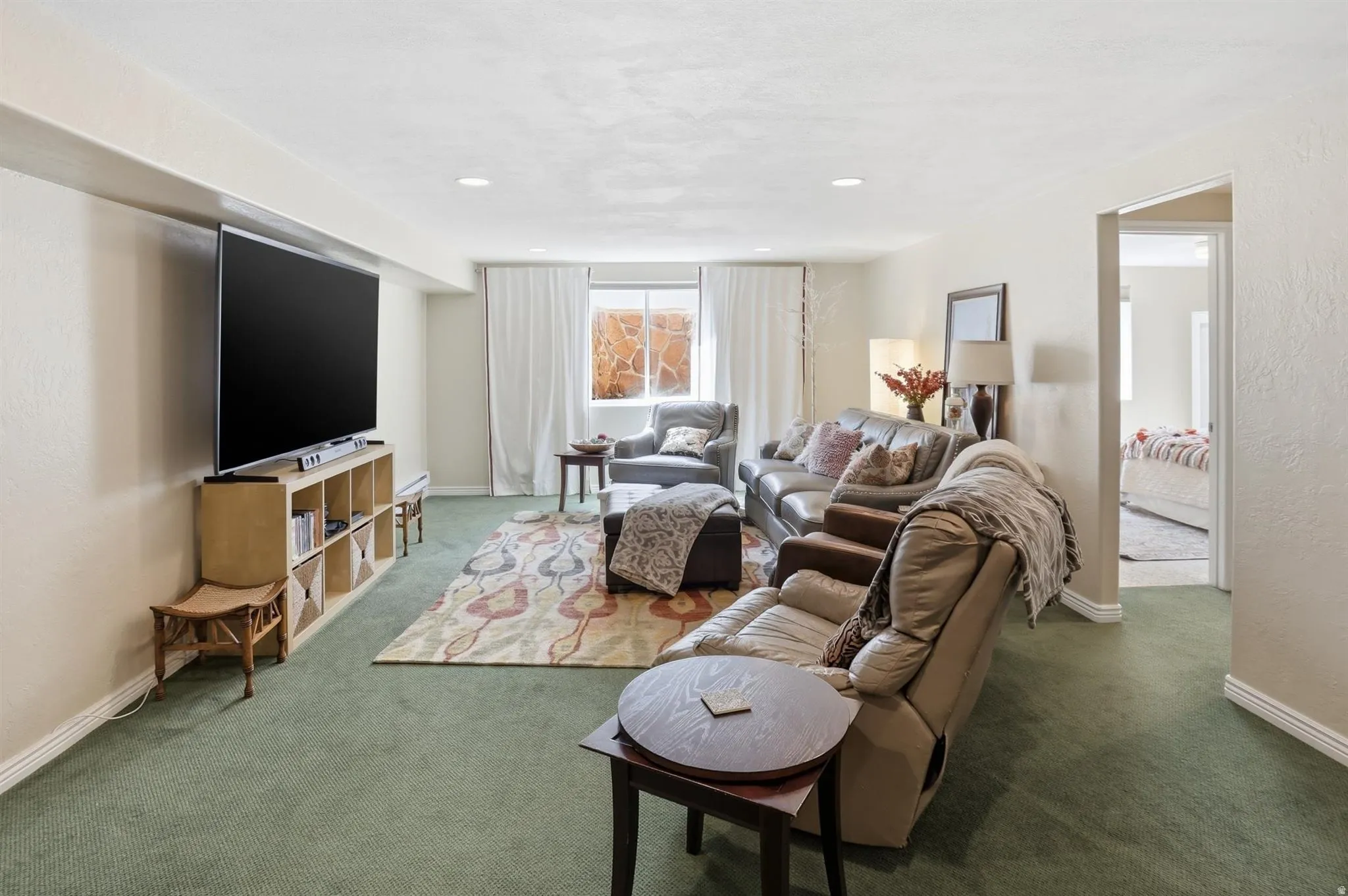 Spacious living area featuring light green carpet and a rectangular area rug with an abstract pattern