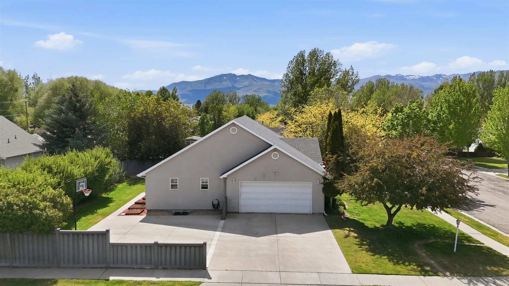 Single-story residence featuring a gray stucco exterior and attached two-car garage and trees