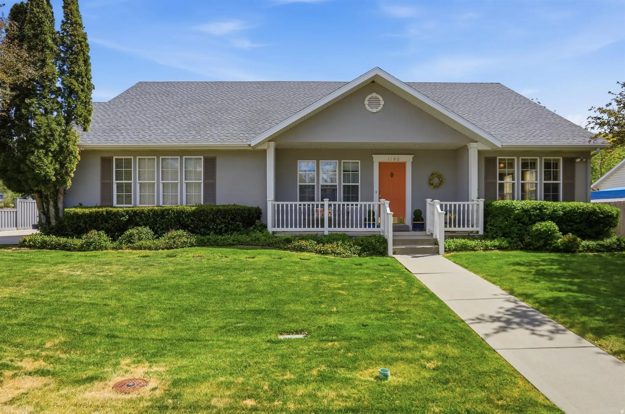 Rambler-style residence featuring a prominent front porch with white railing, a vibrant pink front door, and a light gray exterior