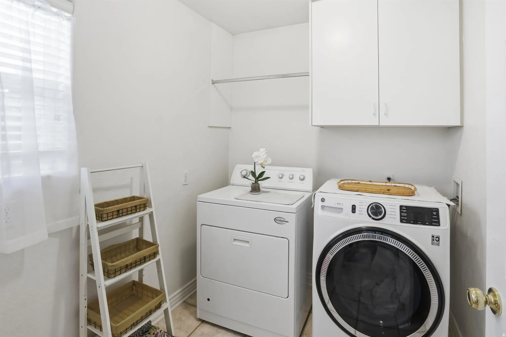 Dedicated laundry room featuring tile flooring, white cabinetry, and a window with blinds. Located off of the kitchen