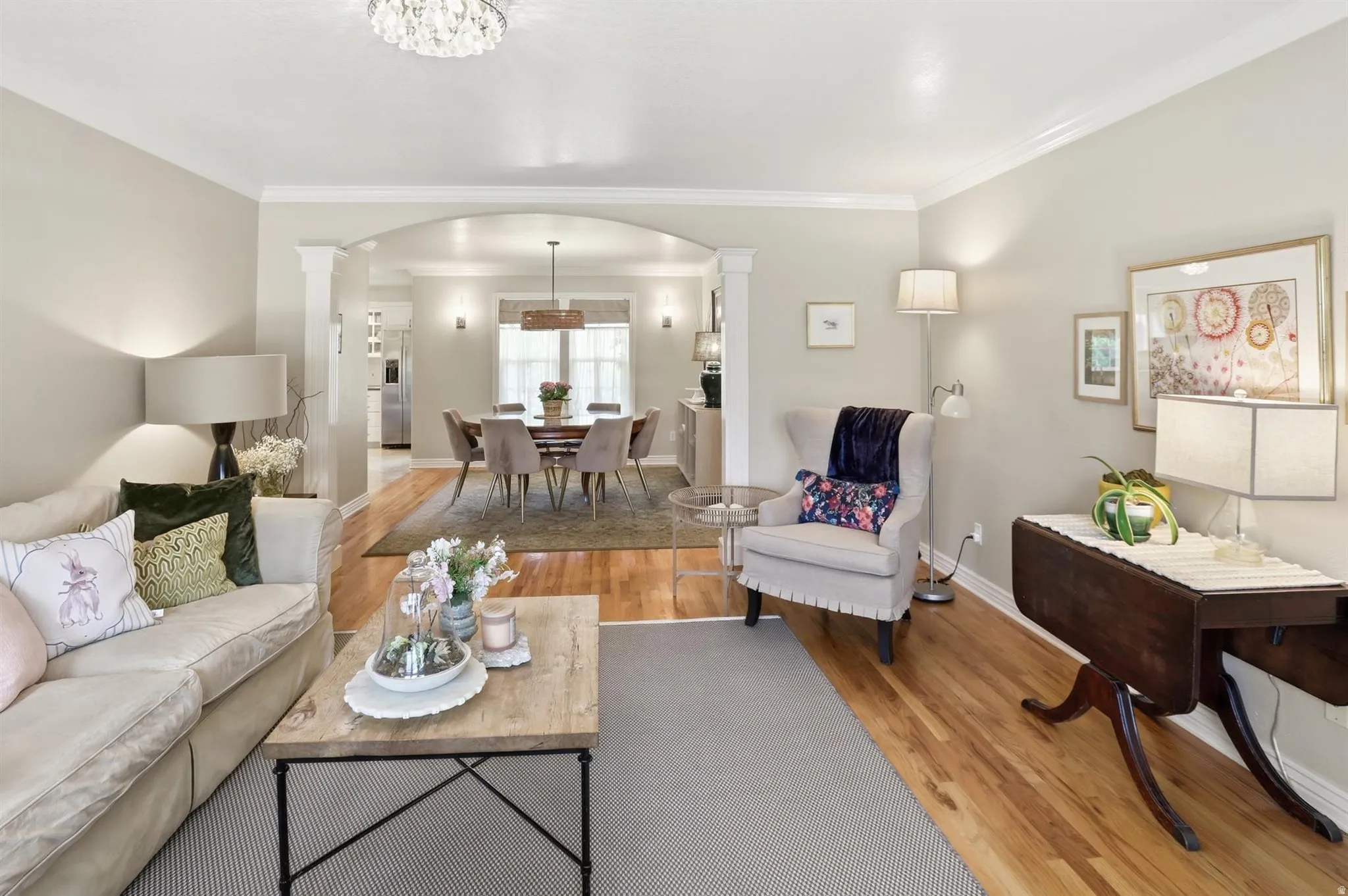 Open-concept living area featuring hardwood flooring, light-colored walls, and crown molding