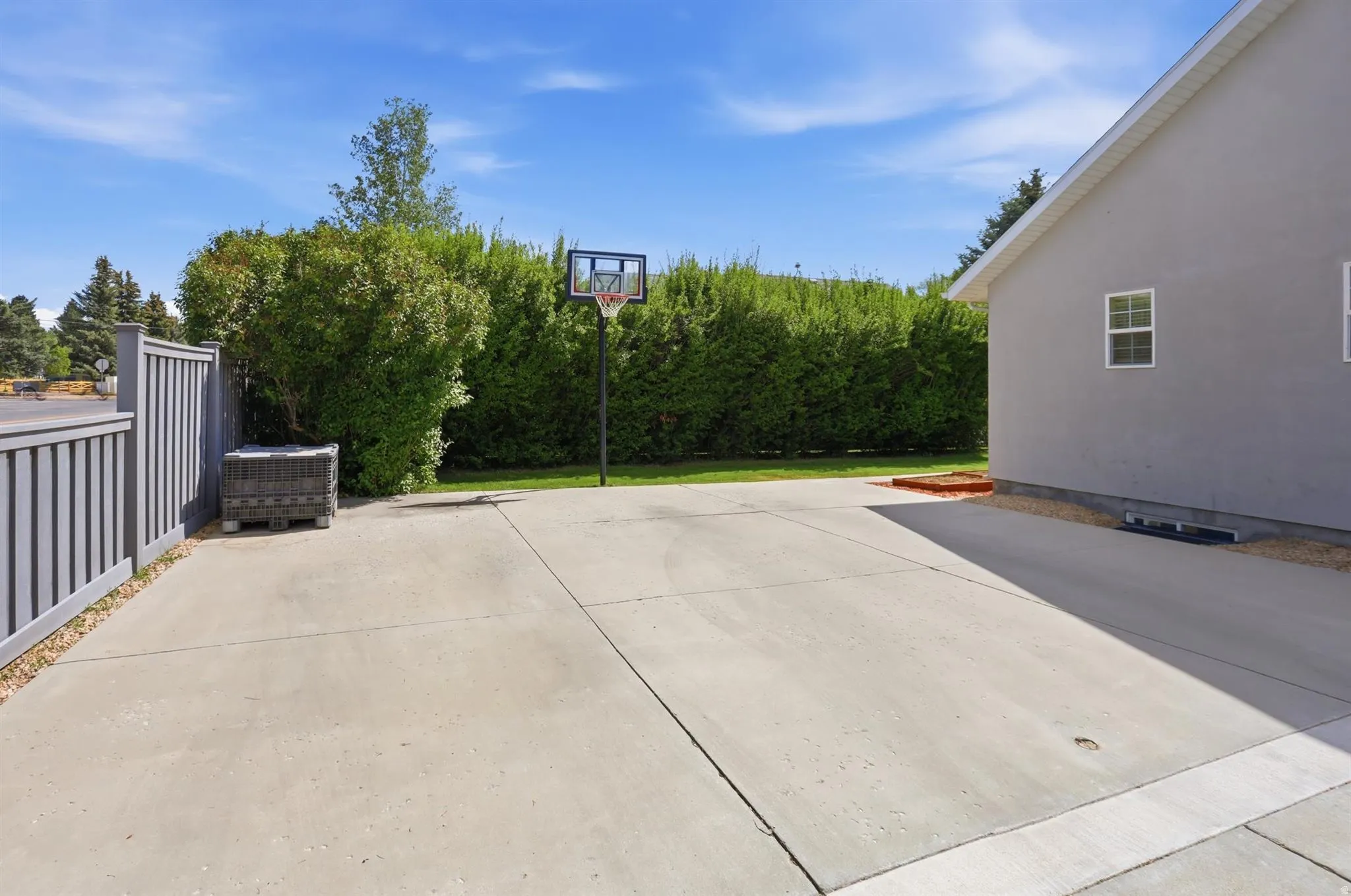 Expansive concrete patio area bordered by a privacy fence and mature hedging