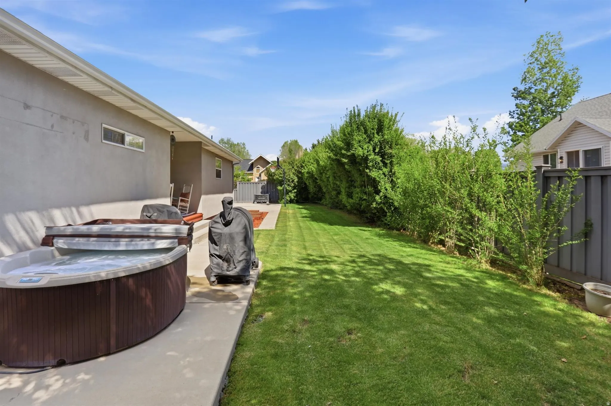 Expansive backyard featuring a concrete patio, a hot tub, and a large lawn area