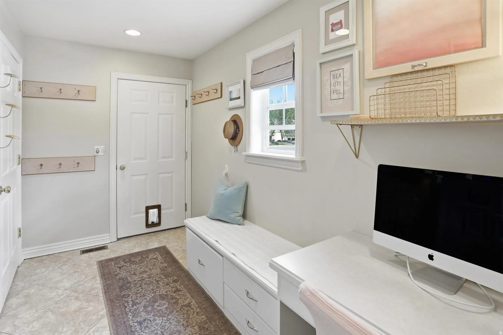 Functional entry space from garage featuring tile flooring, multiple coat hooks, and a built-in bench with storage drawers