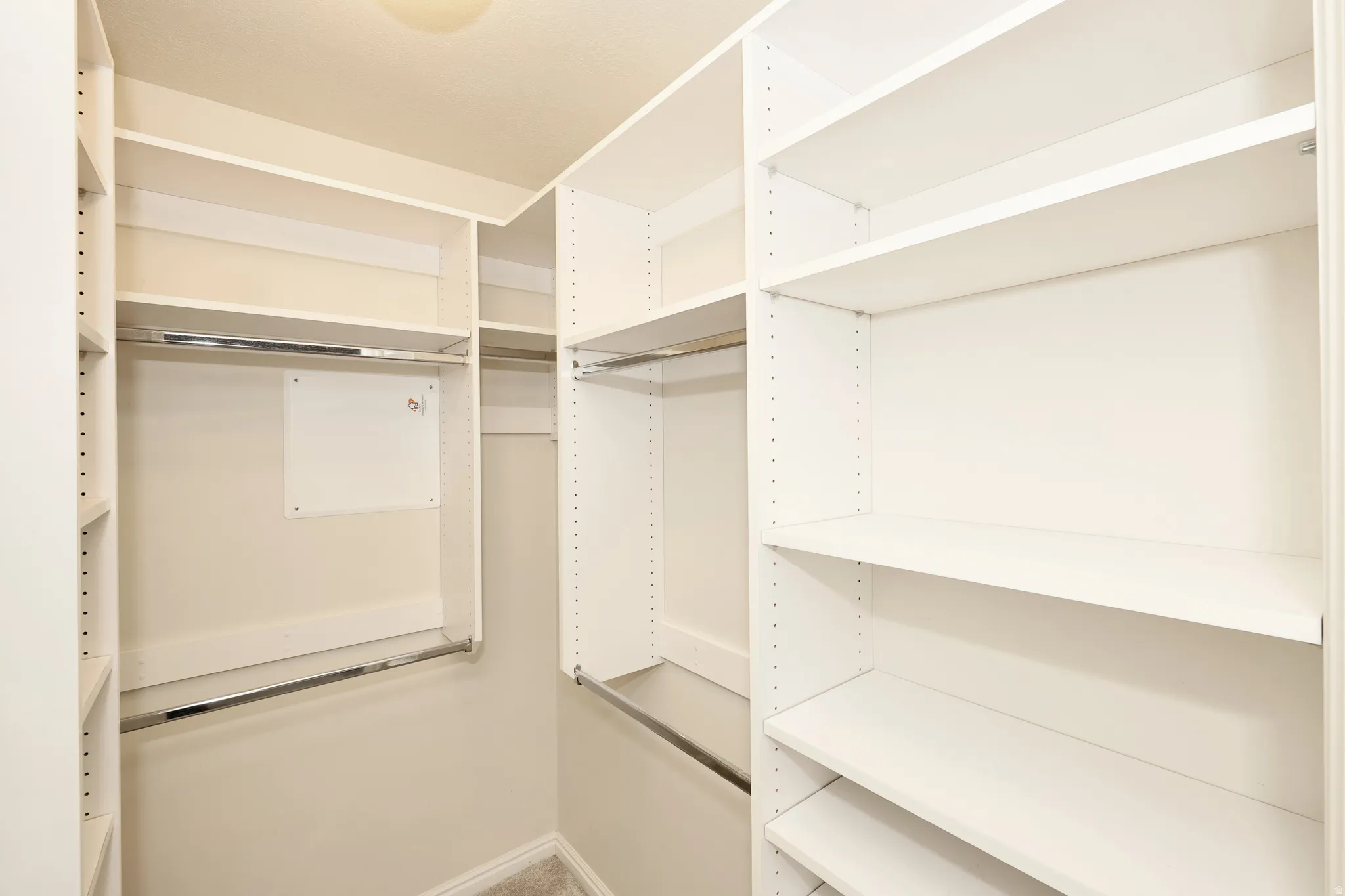 Walk-in closet featuring custom white shelving, multiple hanging rods, and light-toned carpeting