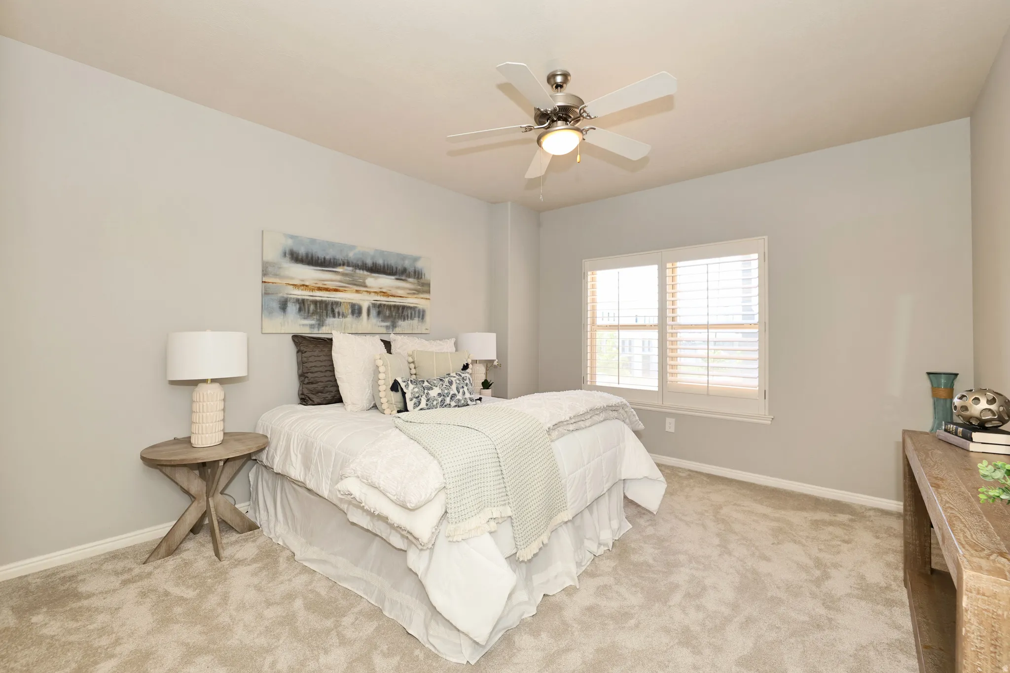 Carpeted bedroom featuring a ceiling fan with integrated lighting, a window with plantation shutters, a light gray wall color, and white baseboards