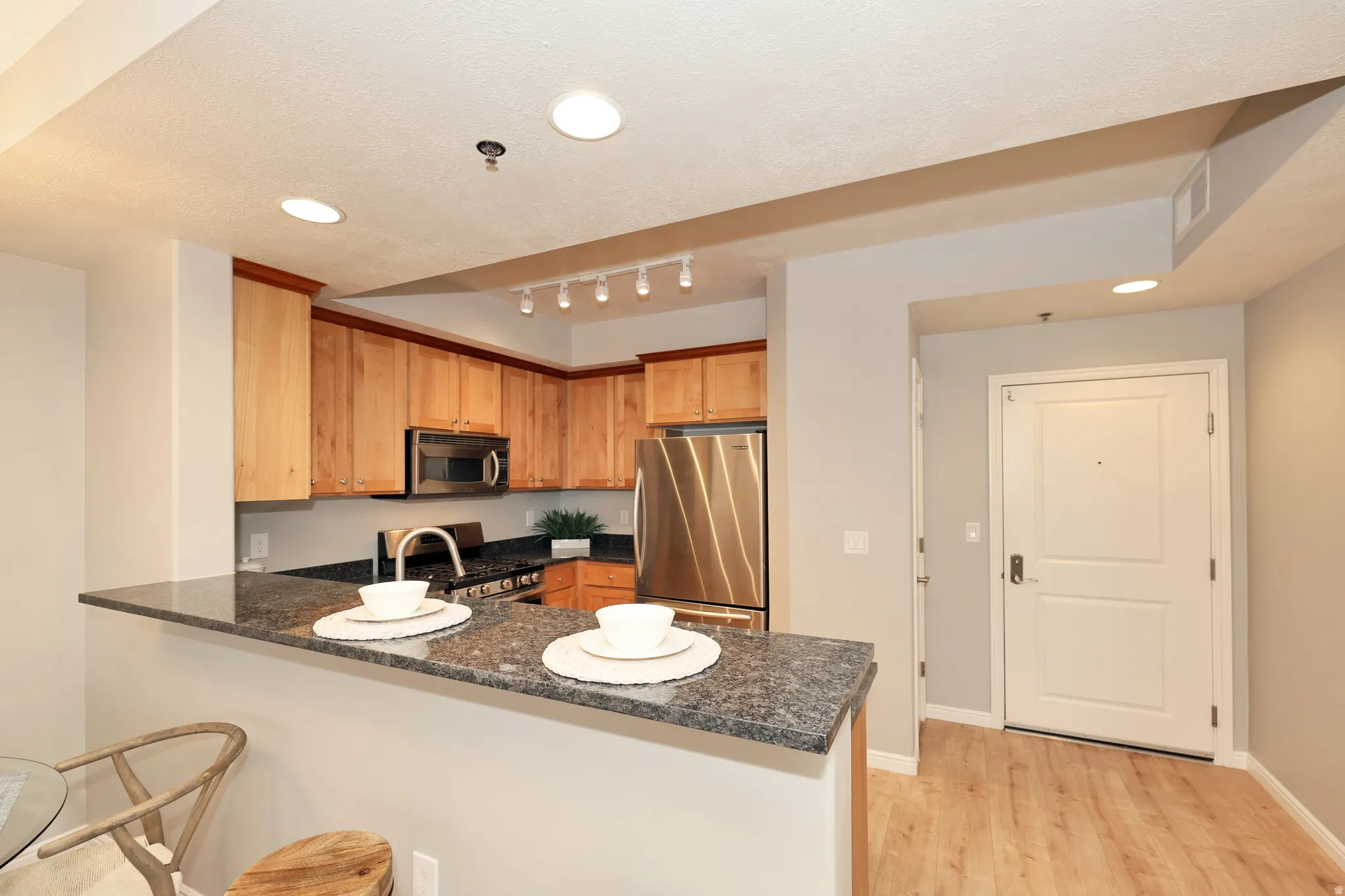 Kitchen featuring wood cabinetry, stainless steel appliances, a dark stone countertop, and an integrated breakfast bar