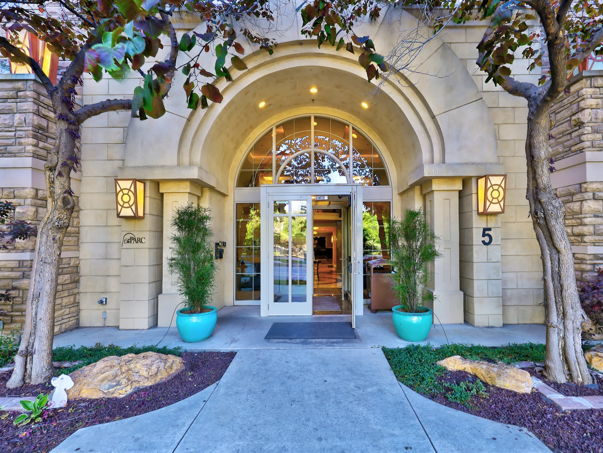 Arched entryway with transom window, flanked by stone veneer and decorative sconces