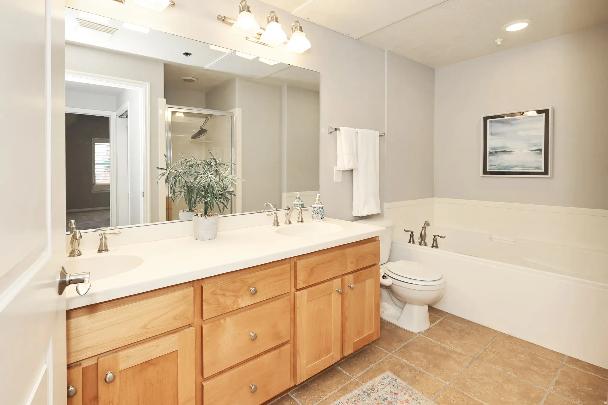 Bathroom featuring a double vanity with light wood cabinetry and dual sinks, a large wall-mounted mirror, a separate shower enclosure with a glass door, and a built-in bathtub with a white surround