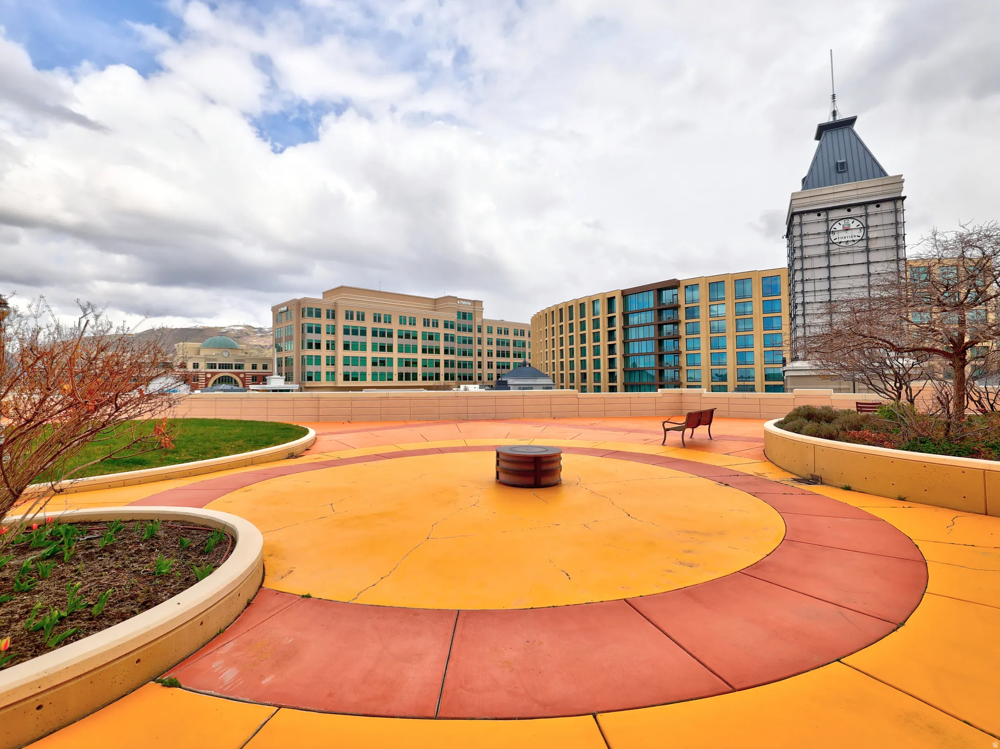 Rooftop amenity space featuring circular paving patterns in orange and red tones, complemented by raised planters with established shrubbery and grass