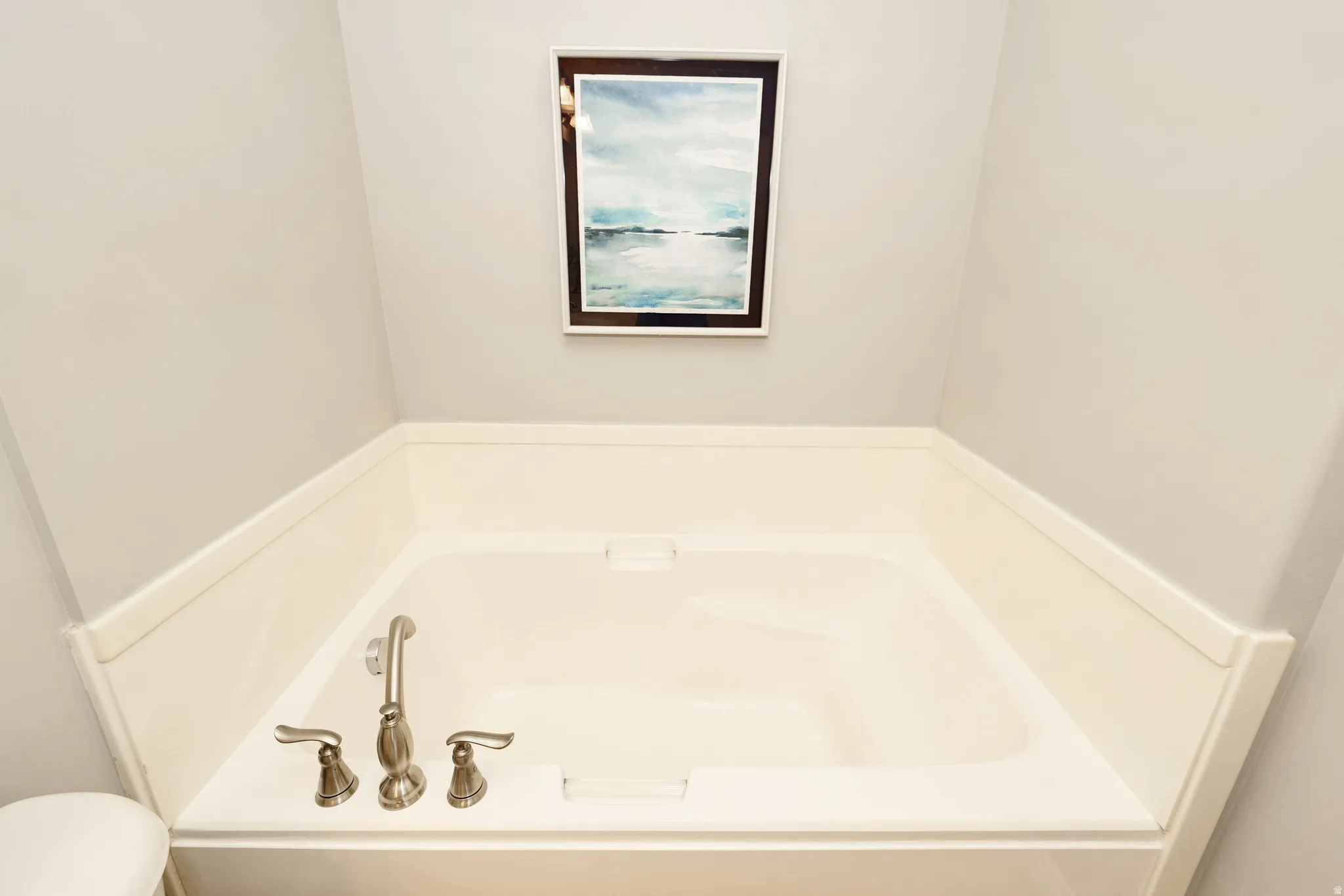 Built-in soaking tub with brushed nickel fixtures and a surrounding white paneling