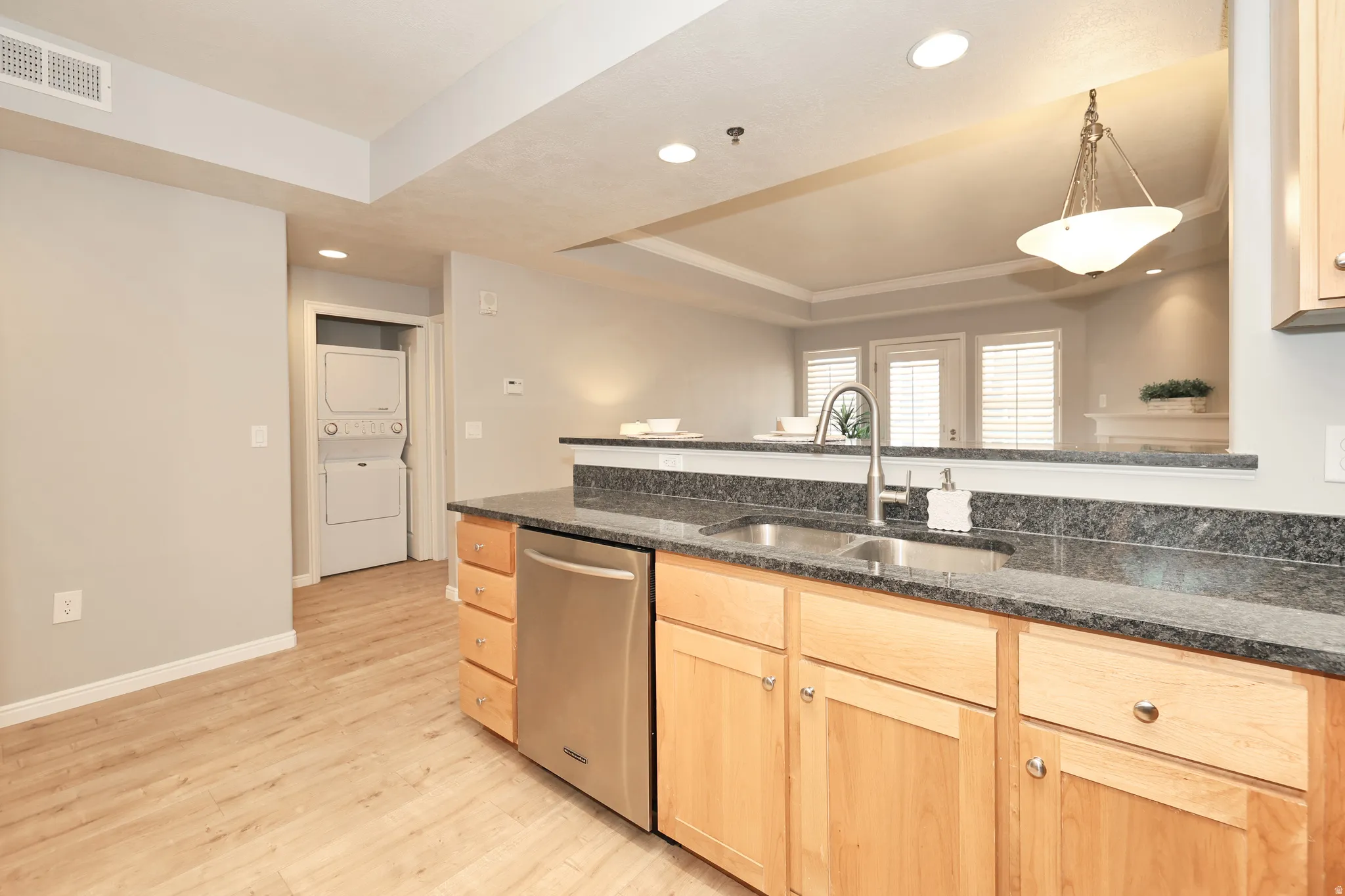 Kitchen featuring a stainless steel sink, dark granite countertops, and light wood cabinetry