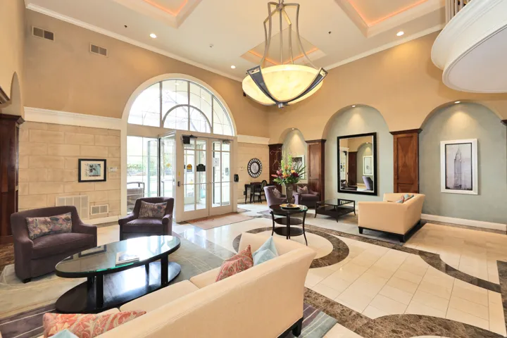Grand foyer featuring a coffered ceiling with a large chandelier, arched doorway with a transom window, floor-to-ceiling stone-look wall treatment, and patterned tile flooring