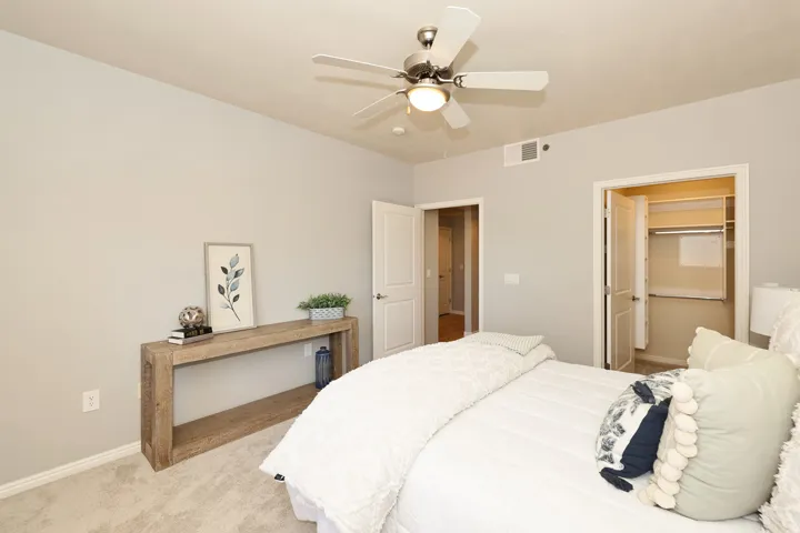 Carpeted bedroom featuring a ceiling fan with integrated lighting, a built-in closet with shelving and hanging rods, light gray walls, and white trim