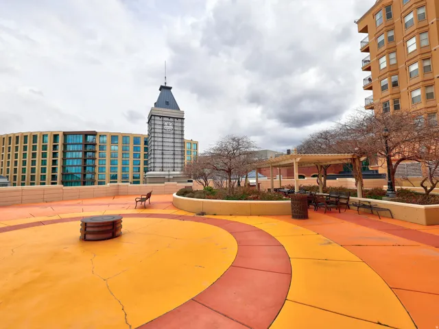 Rooftop patio with vibrant orange and red circular patterns, featuring a pergola-covered seating area, built-in planters, and a central circular fire pit structure