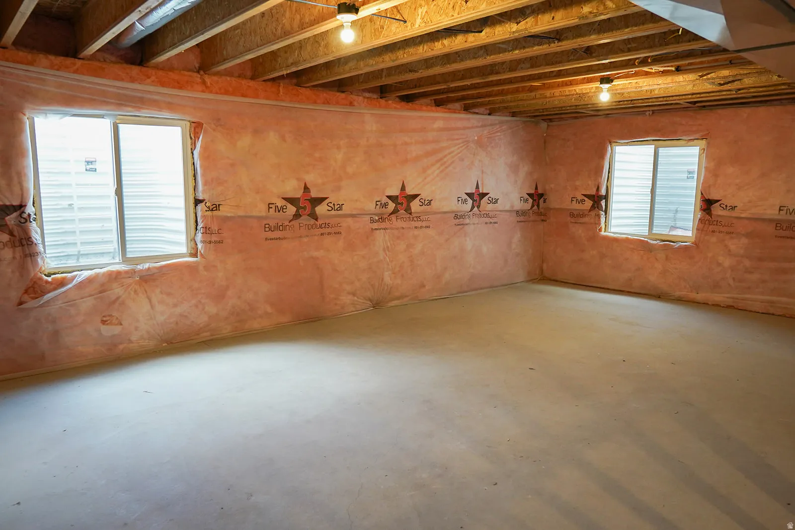 Unfinished lower level with concrete flooring, two egress windows, and exposed ceiling joists