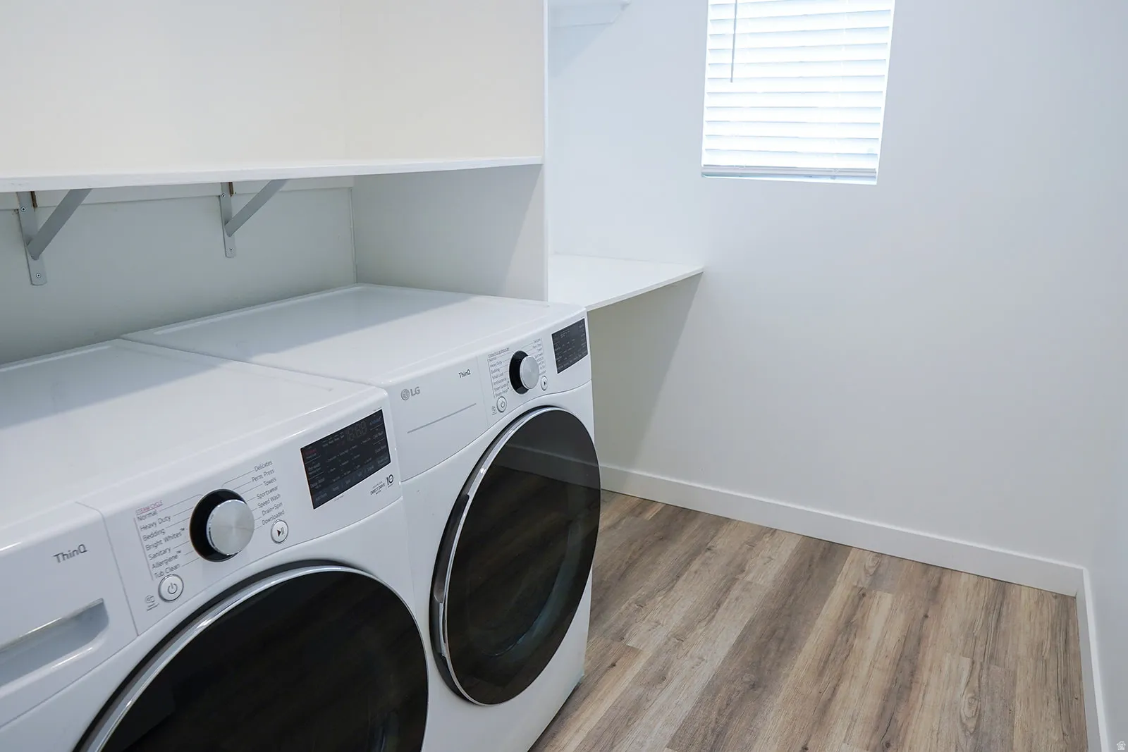 Dedicated laundry area featuring wood-finish flooring, white walls, and a window with blinds