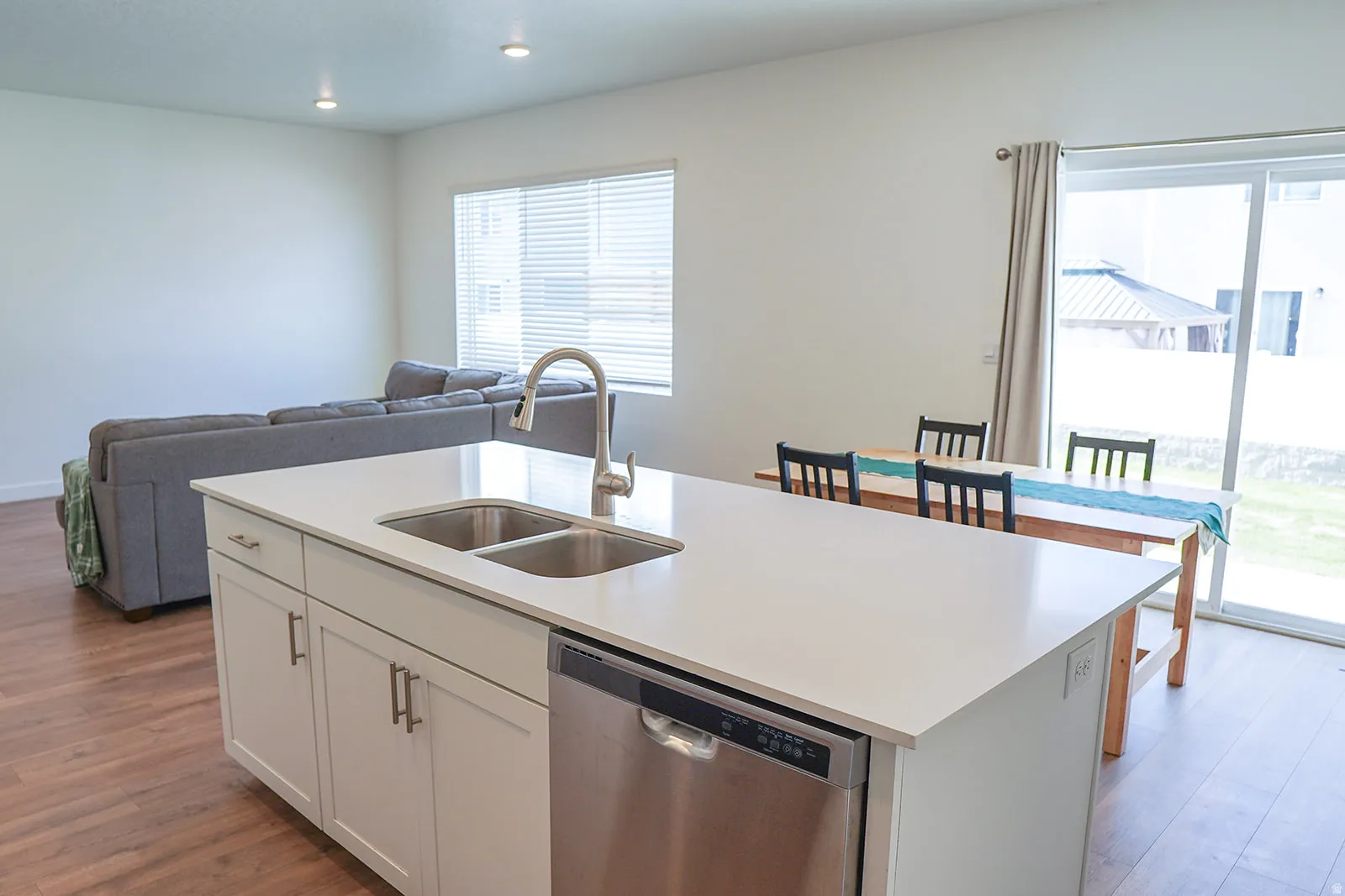 Kitchen island with an undermount double-basin sink, stainless steel faucet, white cabinetry, and a built-in stainless steel dishwasher