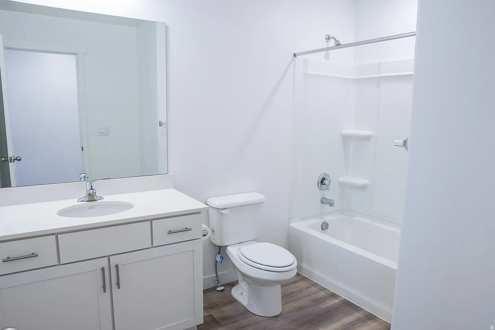 Contemporary bathroom featuring a white vanity with an integrated sink, a large frameless mirror, a white toilet, and a white bathtub with a shower enclosure