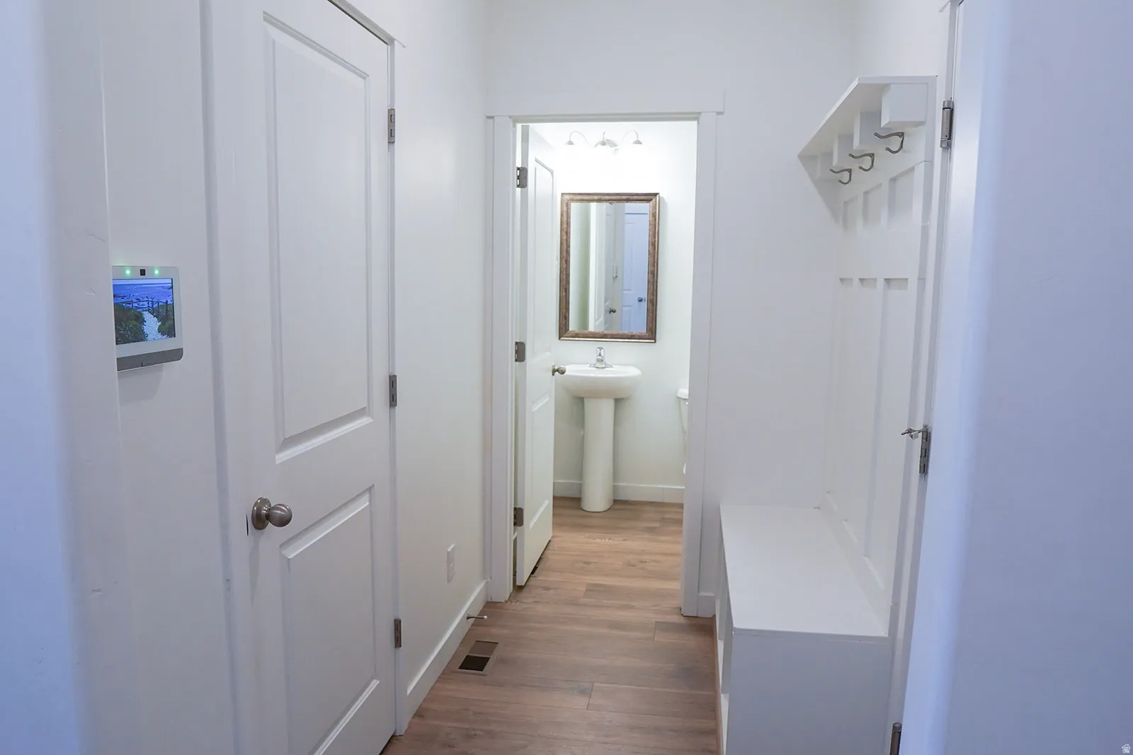 Hallway featuring wood-finish flooring, a built-in hall tree with bench, and access to a bathroom with a pedestal sink and framed mirror